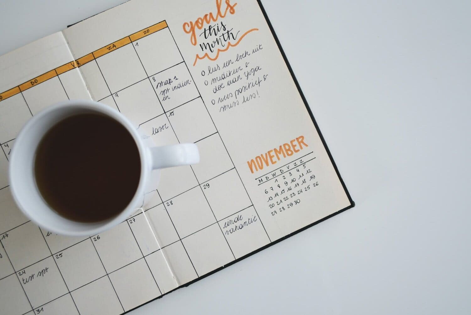 Taza de café llena apoyada sobre una agenda mensual abierta.