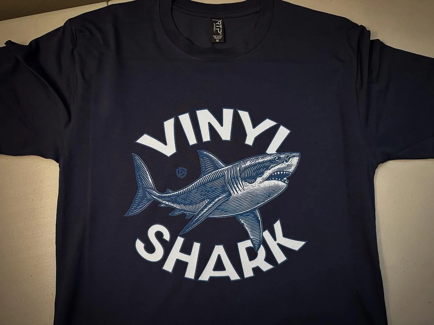 Vinyl Shark 
.
https://goaheadmerch.com/recent-additions/vinyl-shark-tshirt