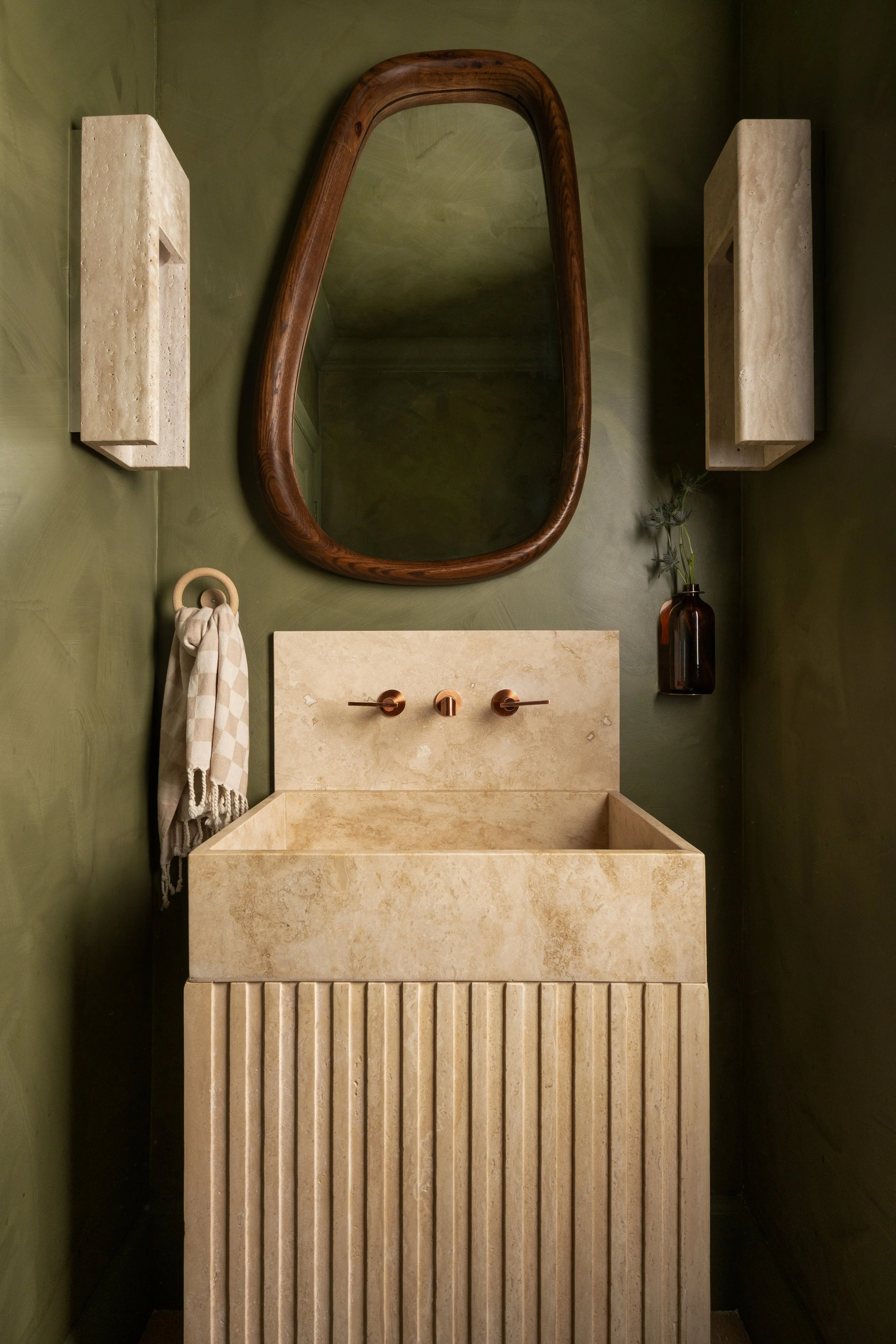 powder room with travertine sink, green lime washed walls, and travertine sconces.
