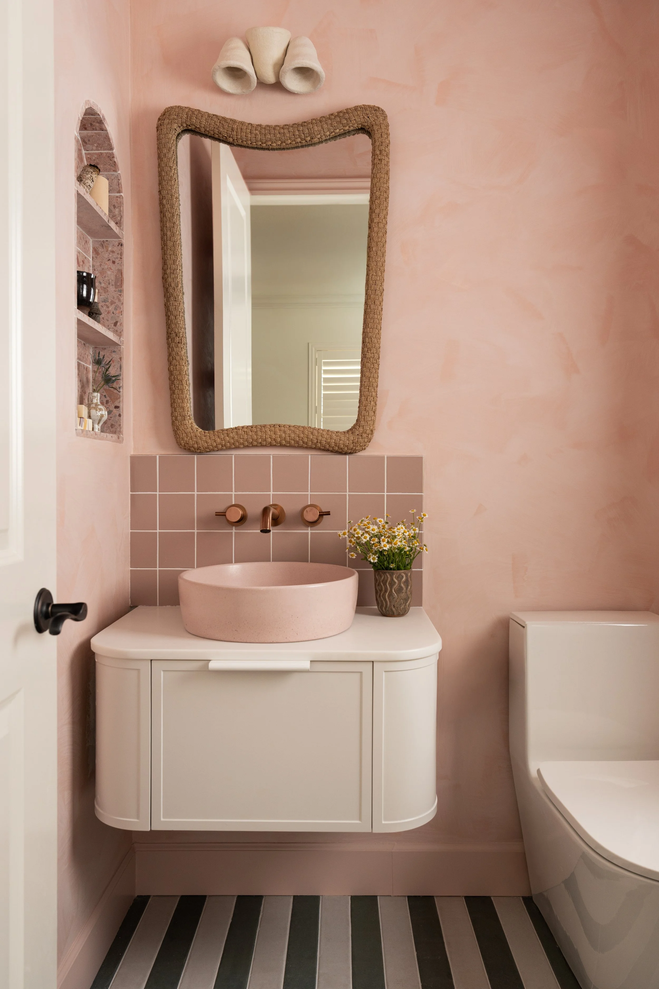 girls bathroom with pink limewashed walls and green and white striped tile.