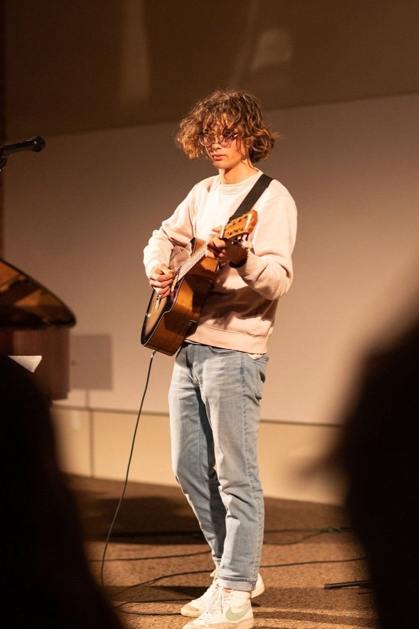  A man with curly hair skillfully strums an acoustic guitar, creating soulful melodies with his fingers. 