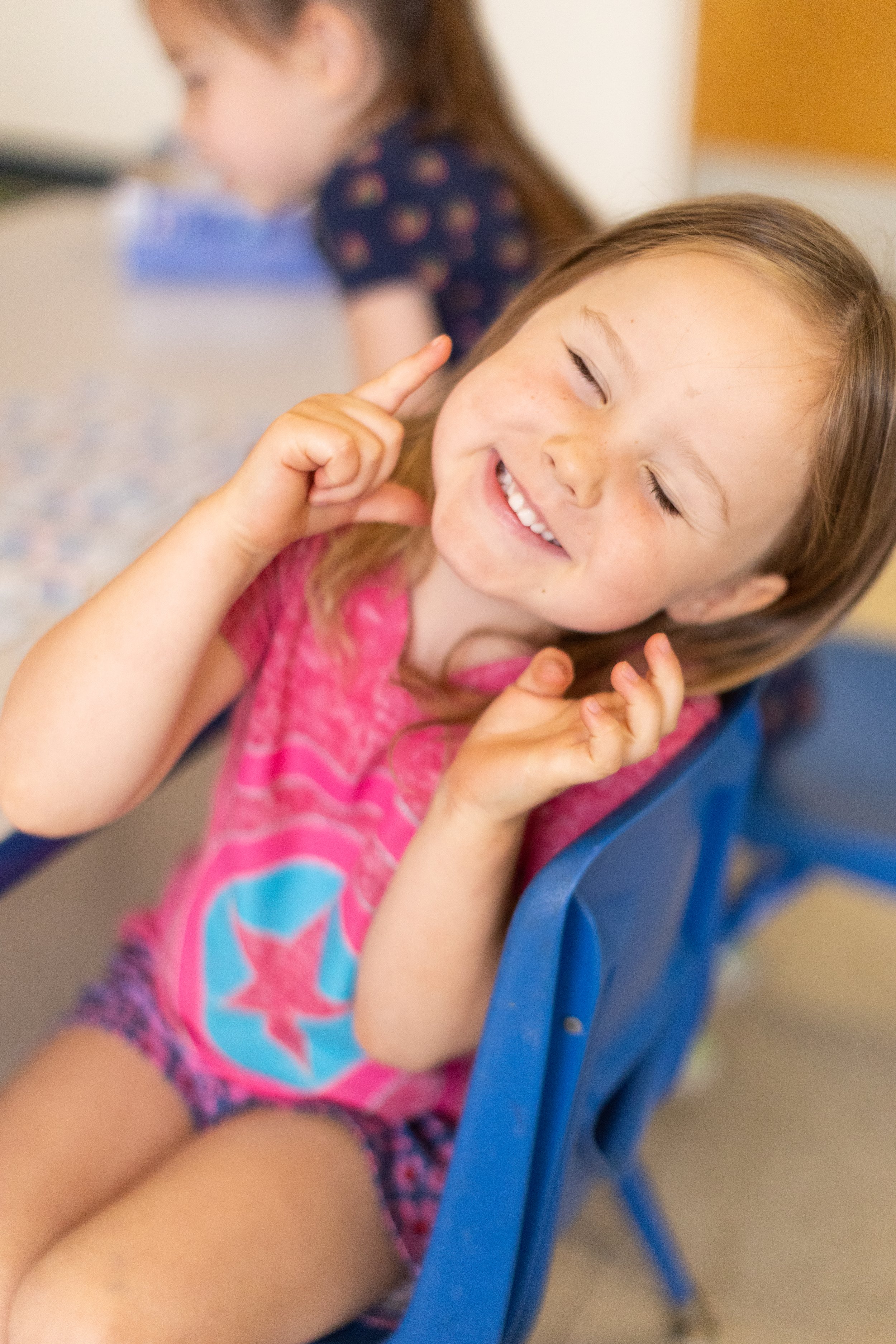  A young girl with a happy expression sitting in a chair with her hands around her face. 