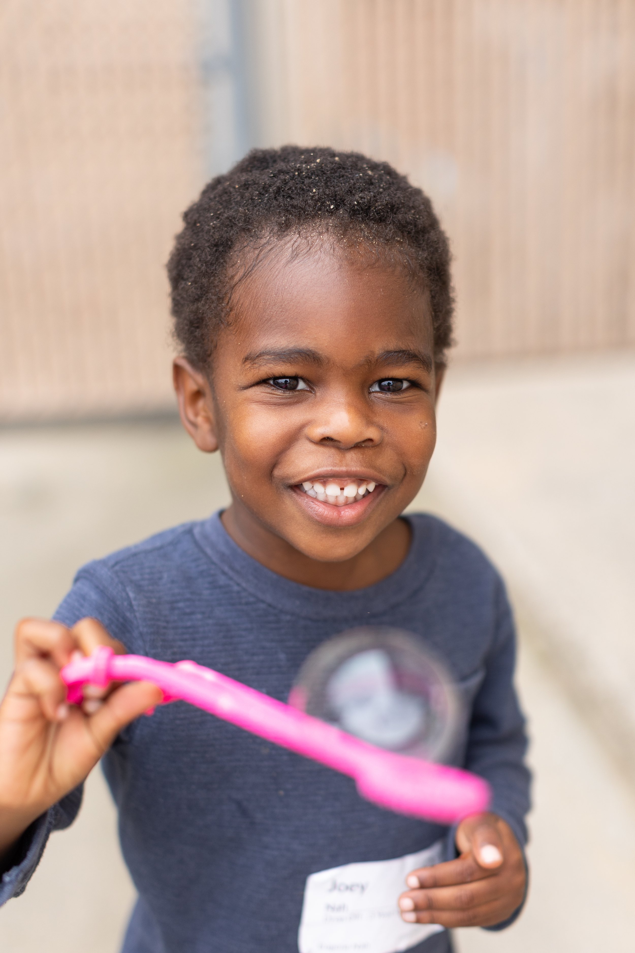  A young boy with a bright smile holds a pink bubble stick 