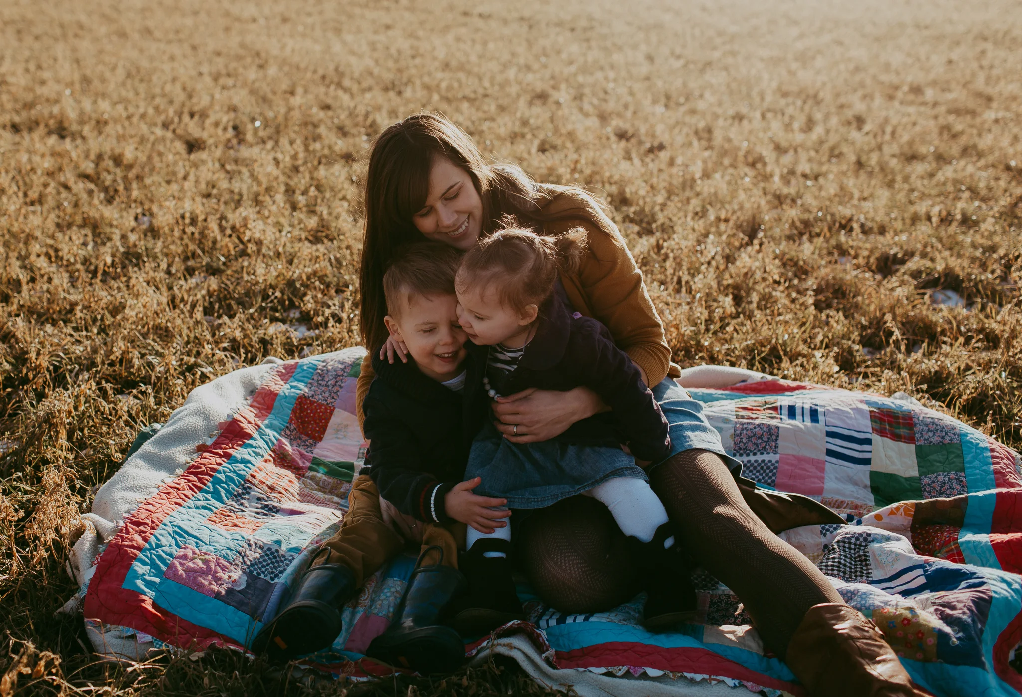 mom cuddling kids on blanket