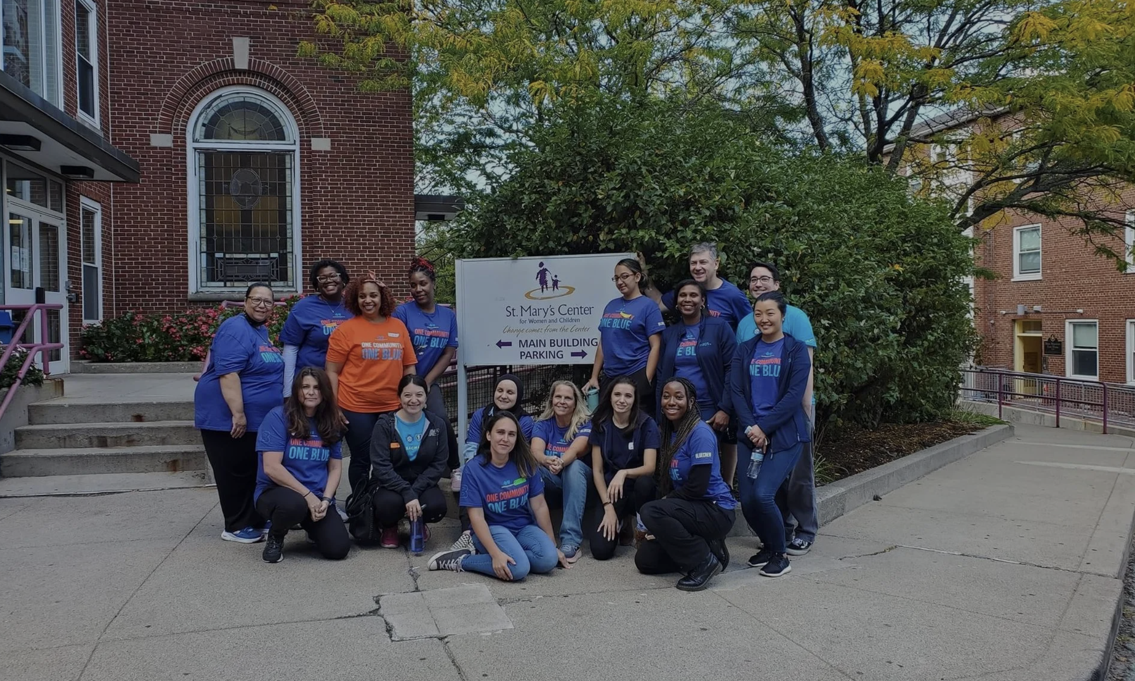A large group of staff and volunteers pose for a photo around the welcome sign outside the SMC building