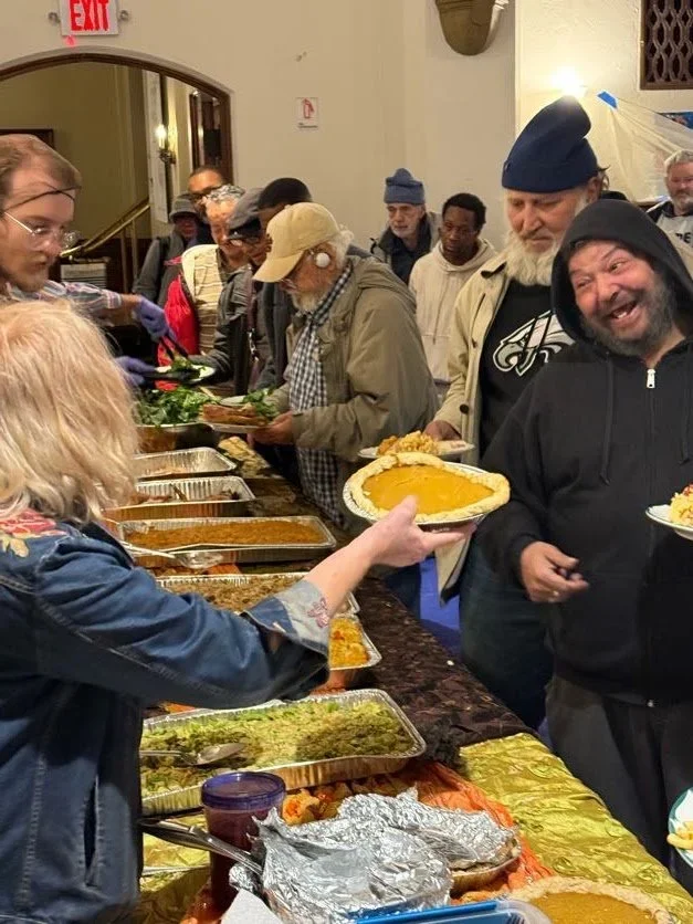A volunteer is handing a guest a whole pumpkin pie, he is smiling at her playfully.