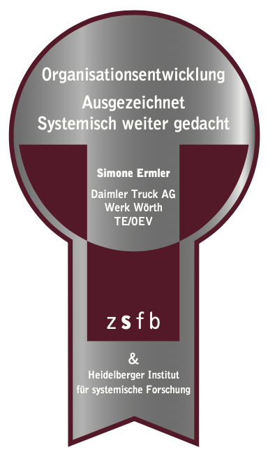Silbernes Emblem mit der Aufschrift "Organisationentwicklung Ausgezeichnet Systemisch weiter gedacht" sowie "Simone Ermler Daimler Truck AG Werk Wörth TE/ØEV" und den Logos von zsfb und dem Heidelberger Institut für systemische Forschung.