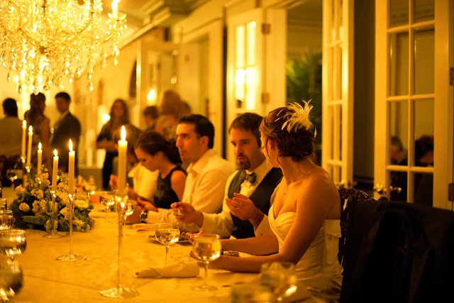 People seated at a wedding reception table with candles, flowers, and elegant decor in a warmly lit room.