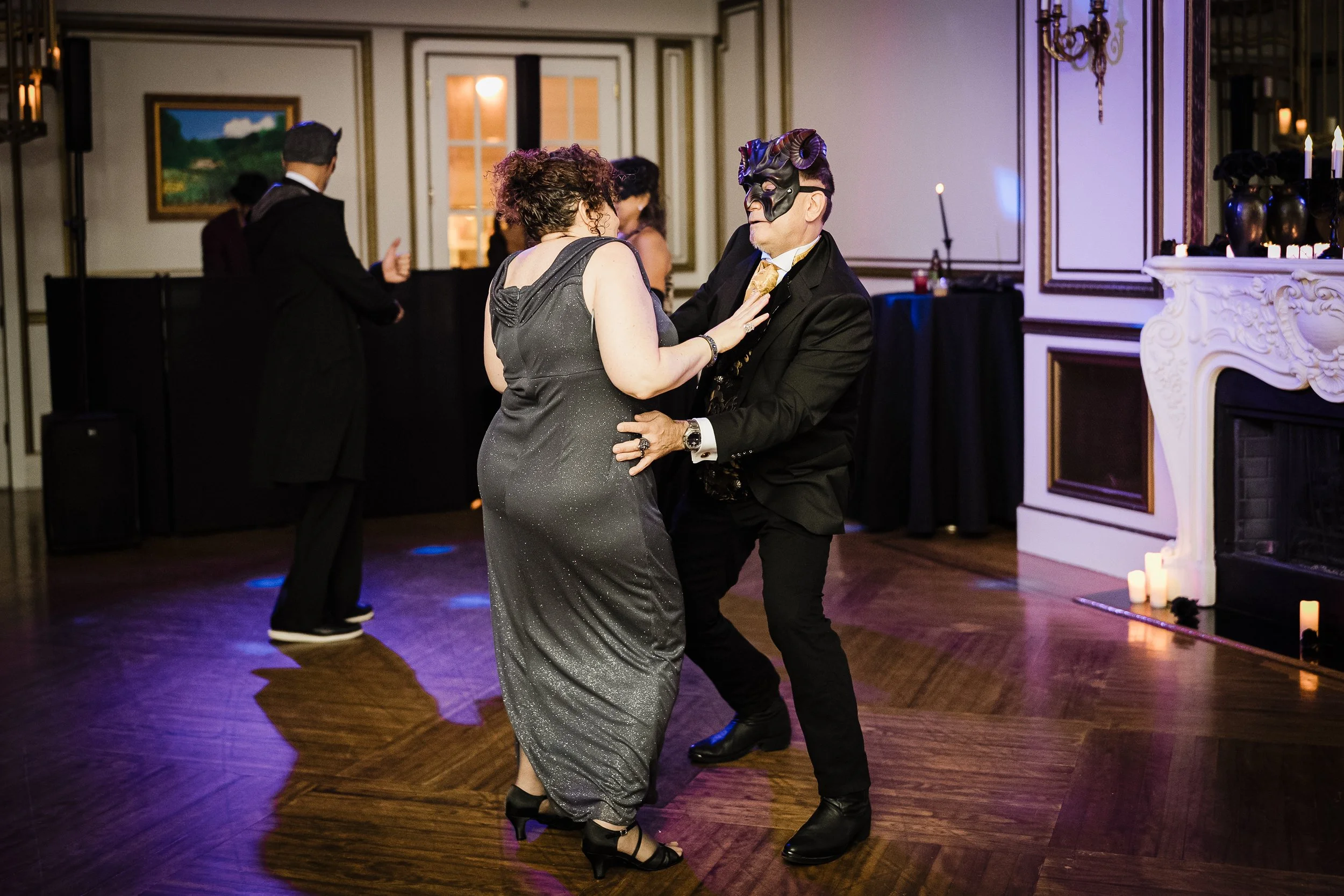 Couple dancing at an elegant indoor event, with candles and classical decor in the background.