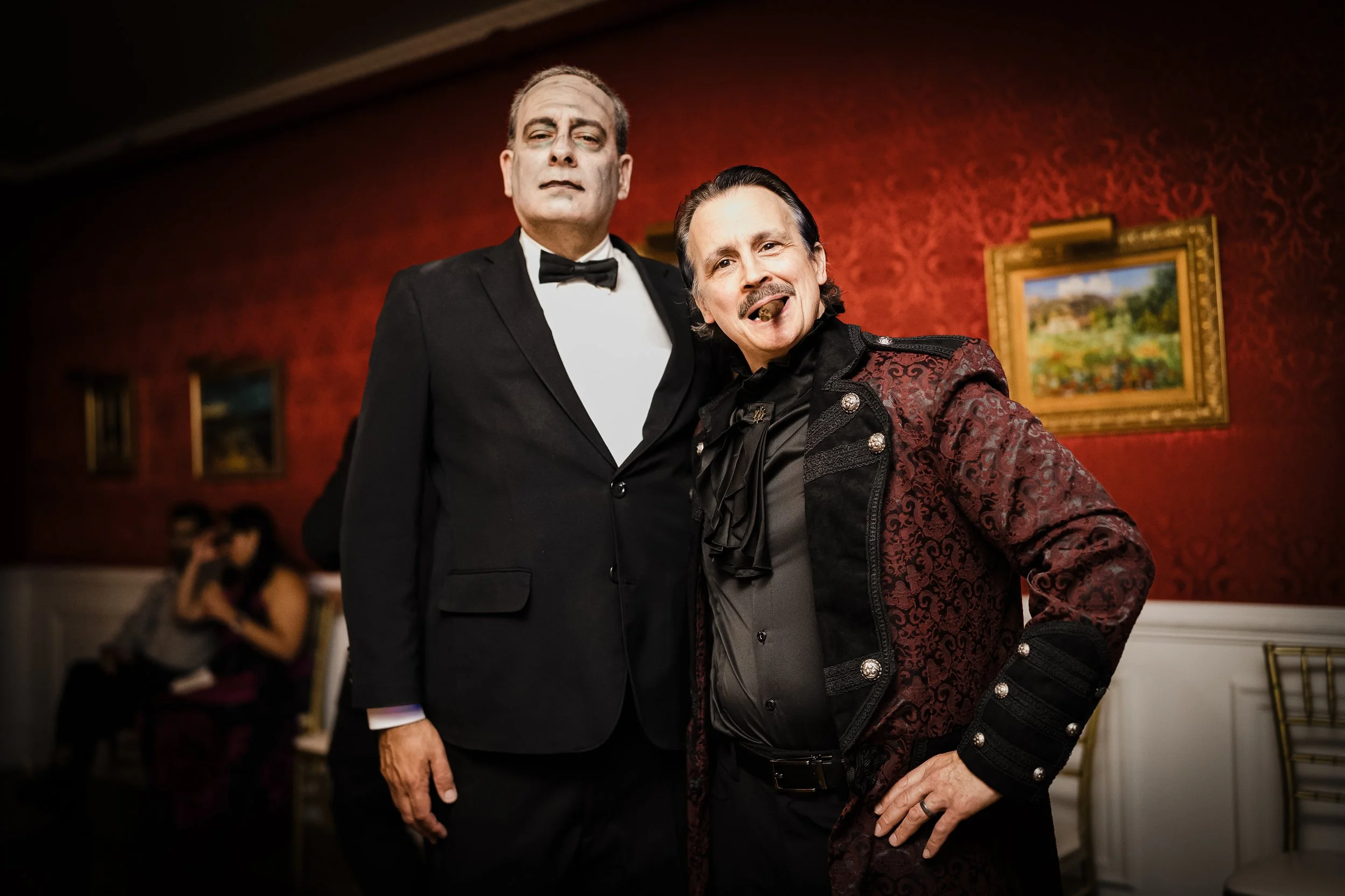Two men dressed in formal tuxedo and ornate jacket posing at an art gallery exhibition.
