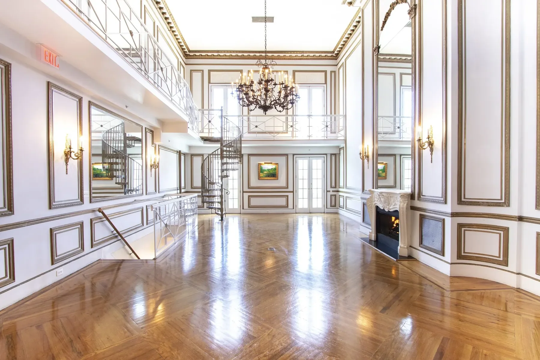 Elegant and spacious room with high ceilings, a large black chandelier, wall sconces, ornate wall paneling, a spiral staircase, and hardwood floors.