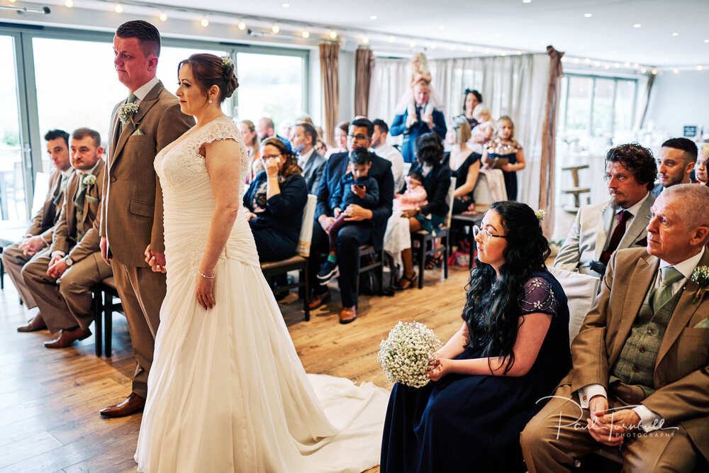 Wedding Photographer The Fleece, Bride and Groom Hold Hands During Ceremony while Guests Watch