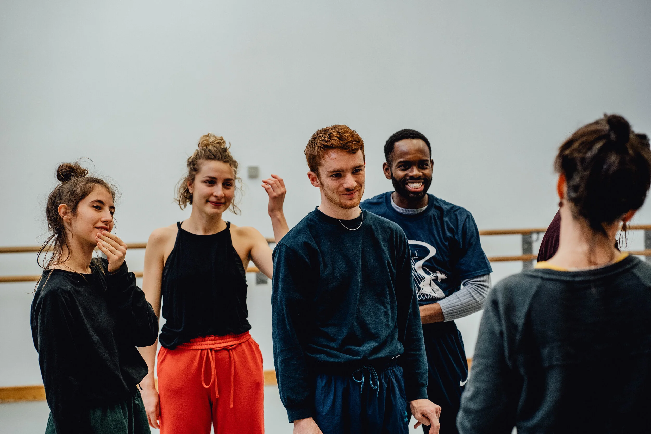 Group of five young adults in dance class, smiling and talking to instructor in dance studio.