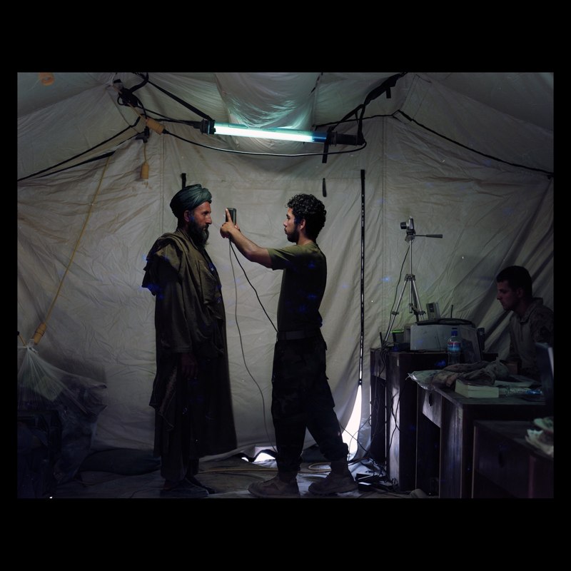  Afghan linguist working for US Marine Civilian Affairs unit doing a retinal scan of a Marja villager who has come to pick up bags of wheat. The villagers are given a retinal scan, photographed and their fingerprints are entered into a national datab