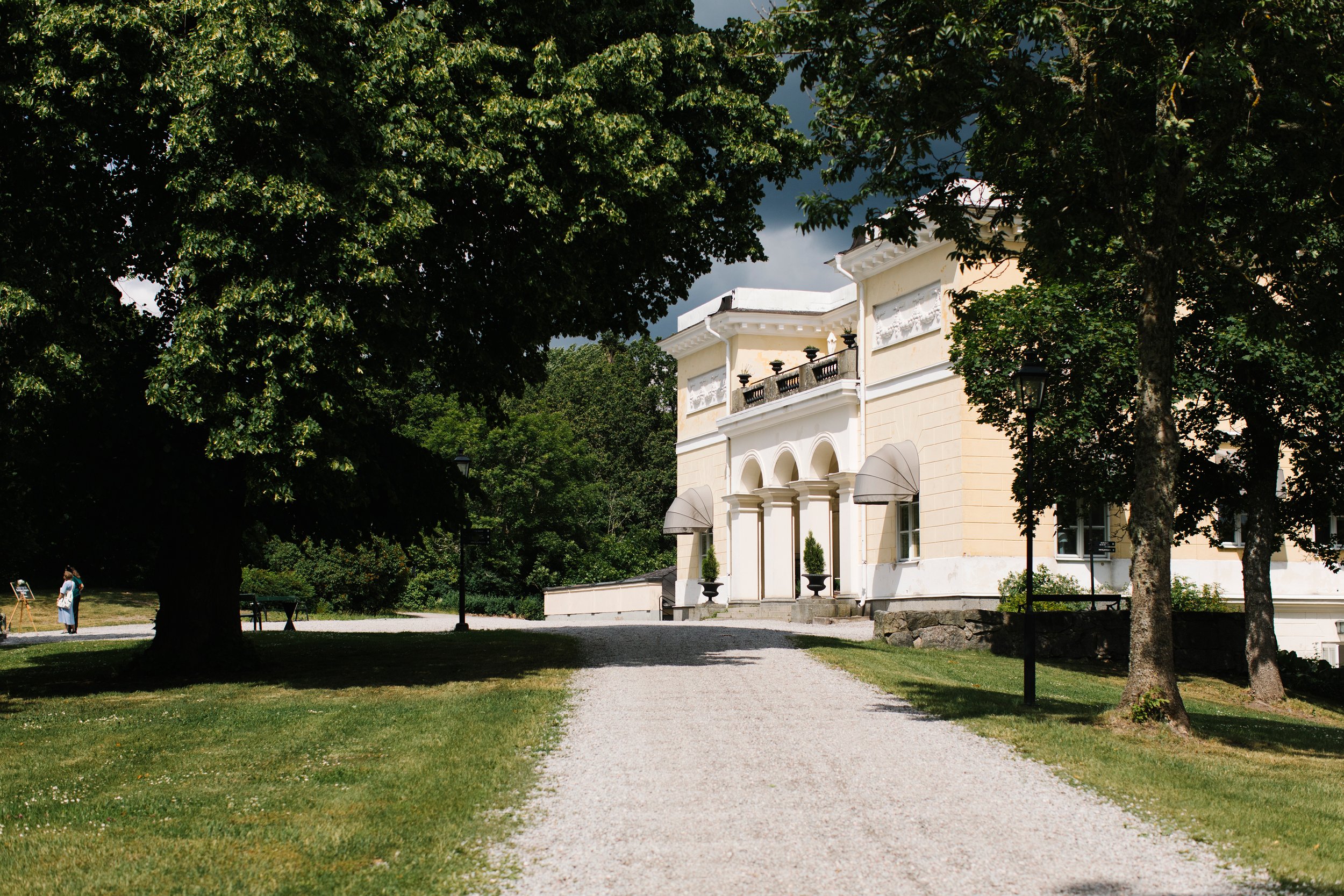 Historic building surrounded by trees with a gravel path leading towards it