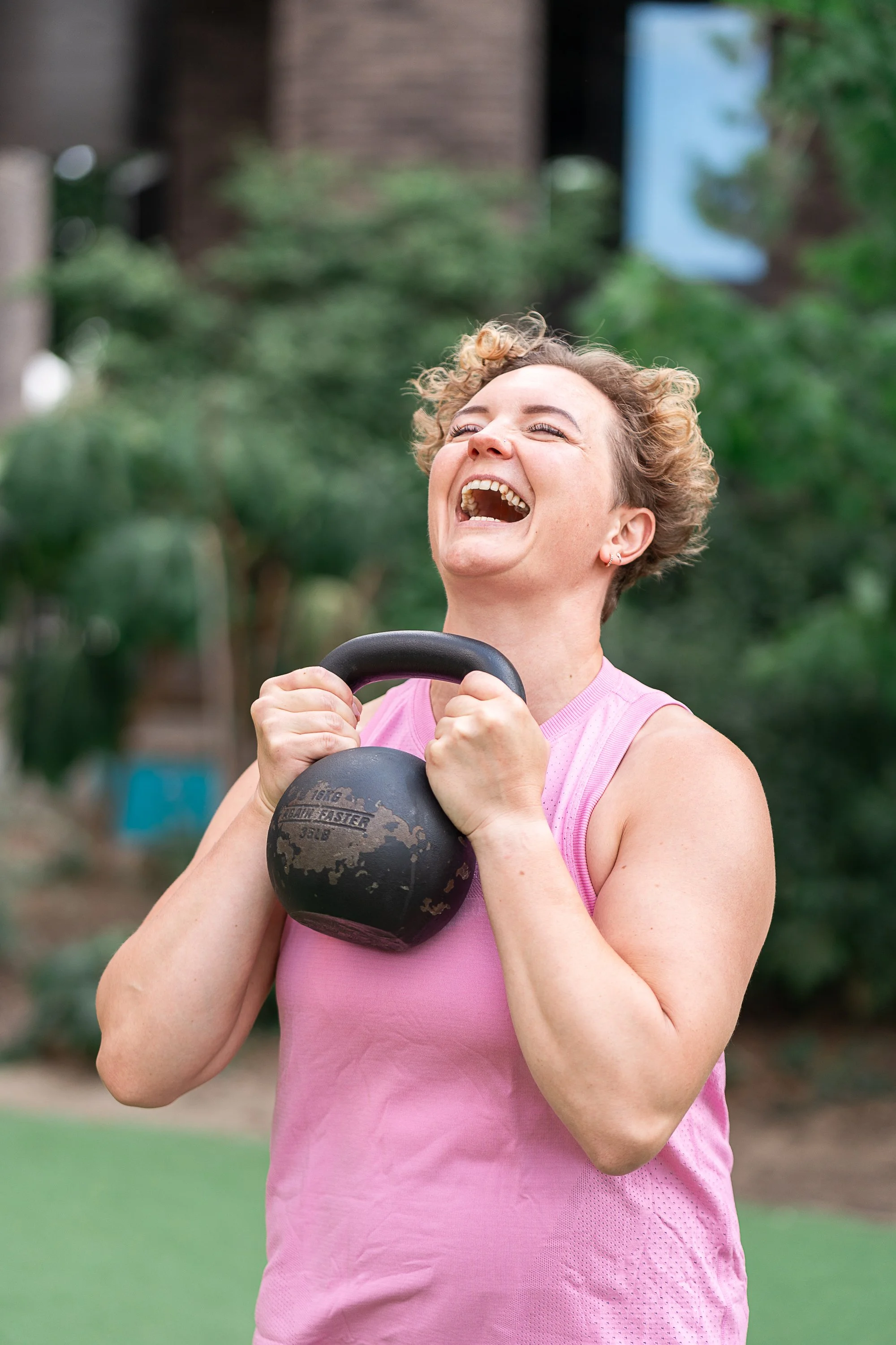 Personal trainer Rowena Ramsell smiling while holding a kettlebell during an outdoor strength training session