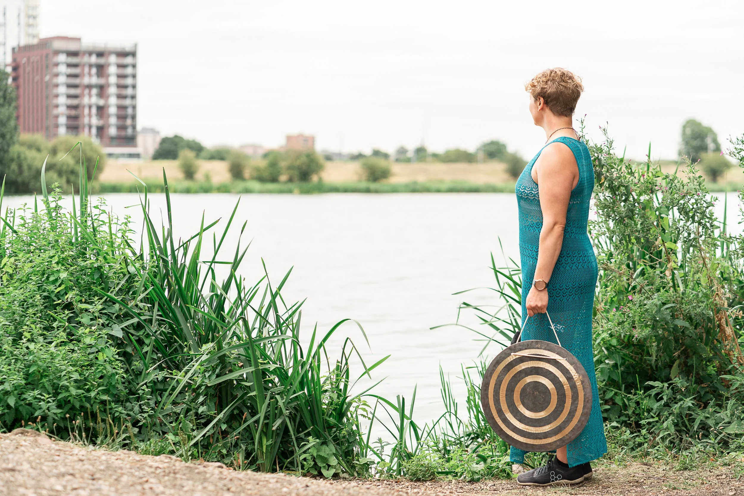 Sound bath facilitator Rowena Ramsell carrying a sound healing instrument beside a London reservoir