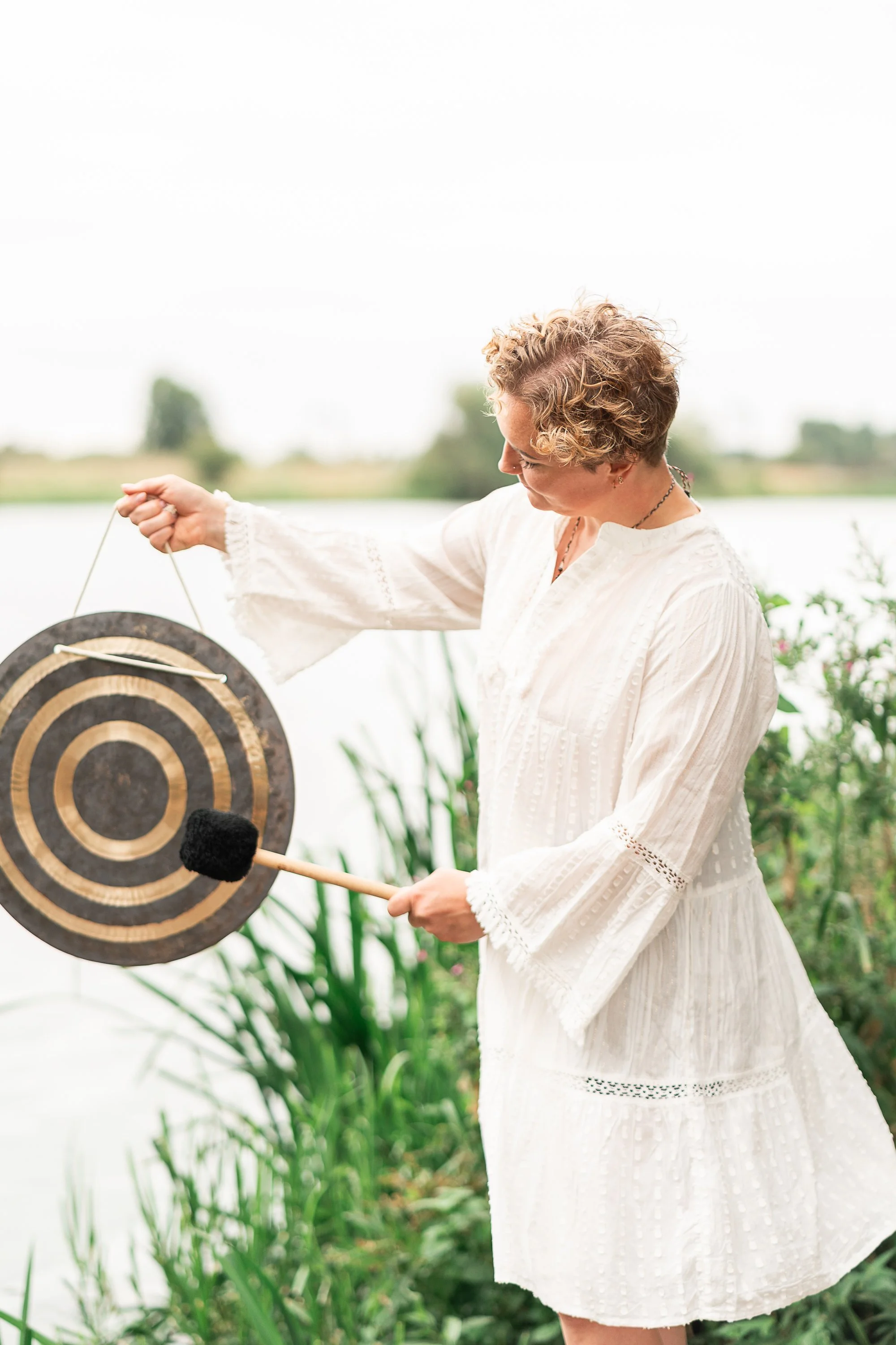 Sound bath facilitator Rowena Ramsell playing a gong beside the water in North London