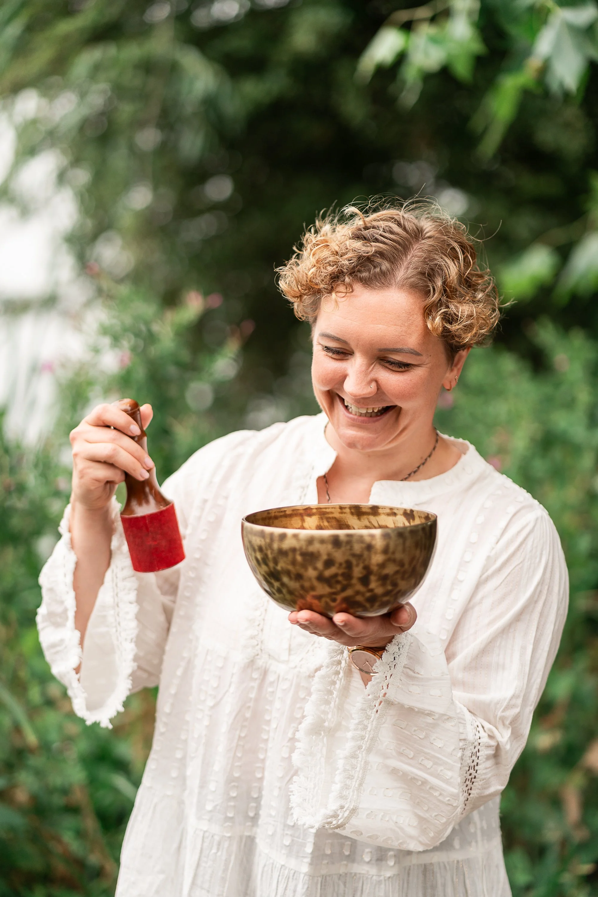 Rowena Ramsell smiling while holding a Tibetan singing bowl and red mallet outdoors