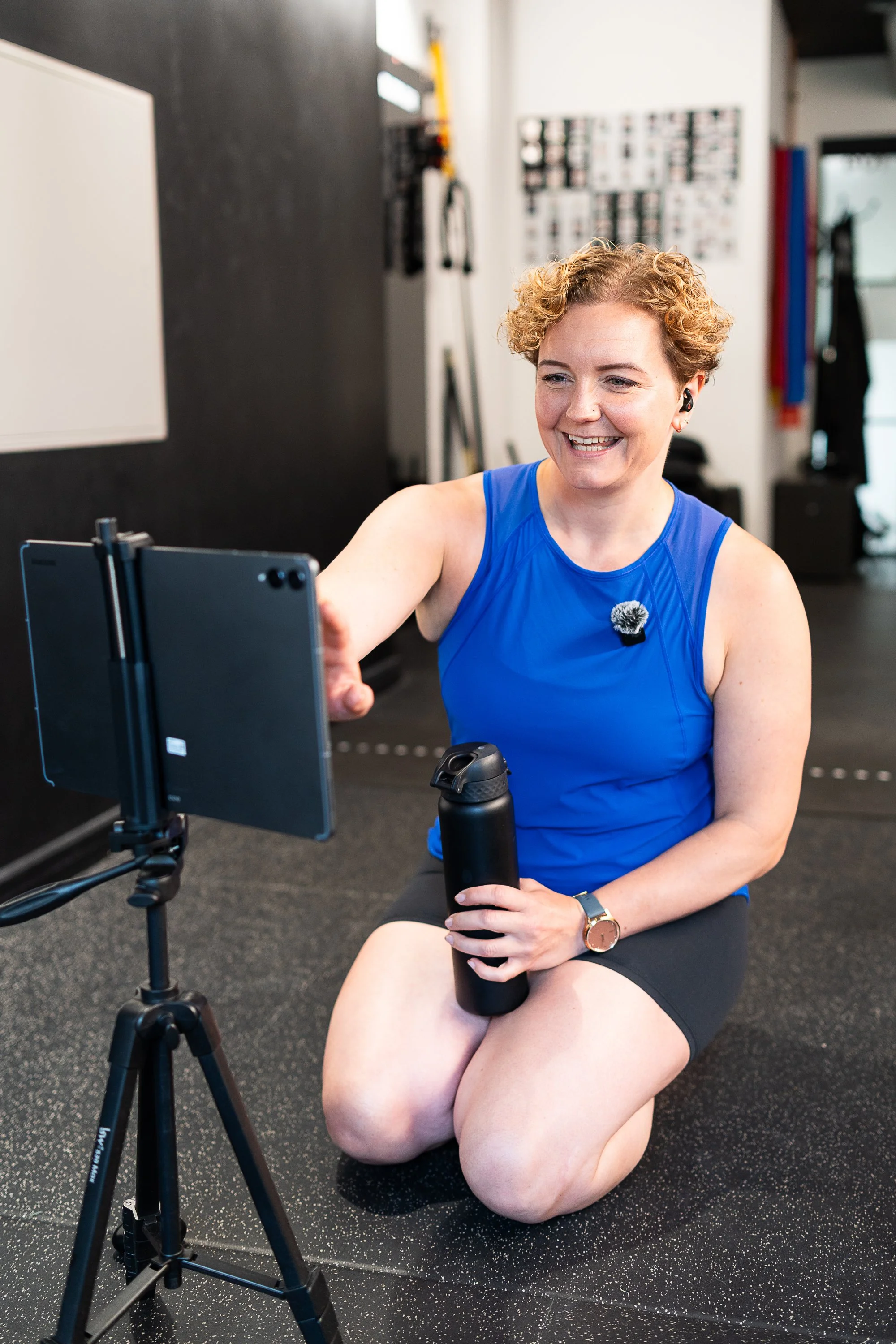 Fitness coach Rowena Ramsell smiling while setting up an online training session in her London gym