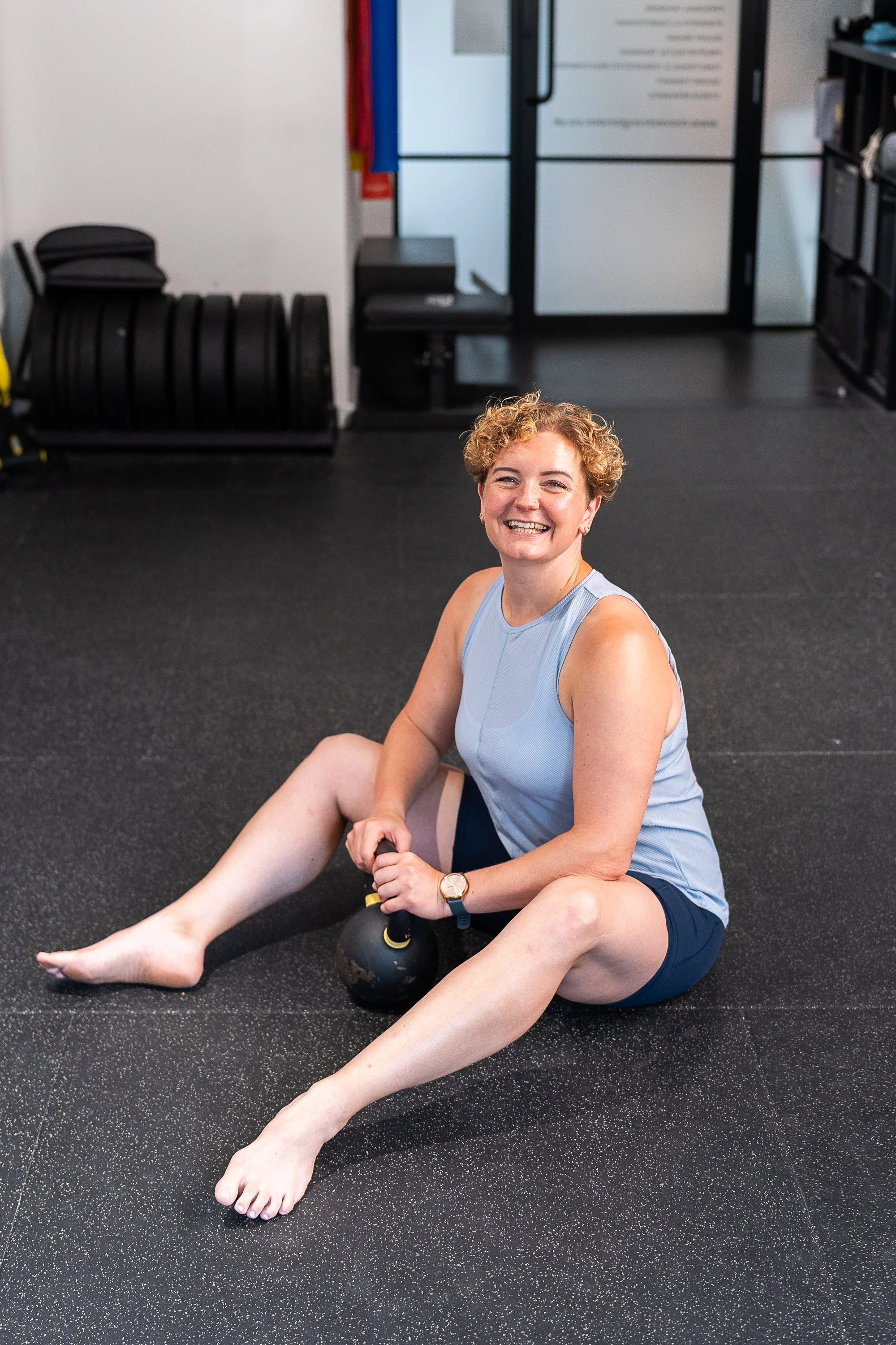 Fitness instructor Rowena Ramsell smiling while sitting on the gym floor beside a kettlebell