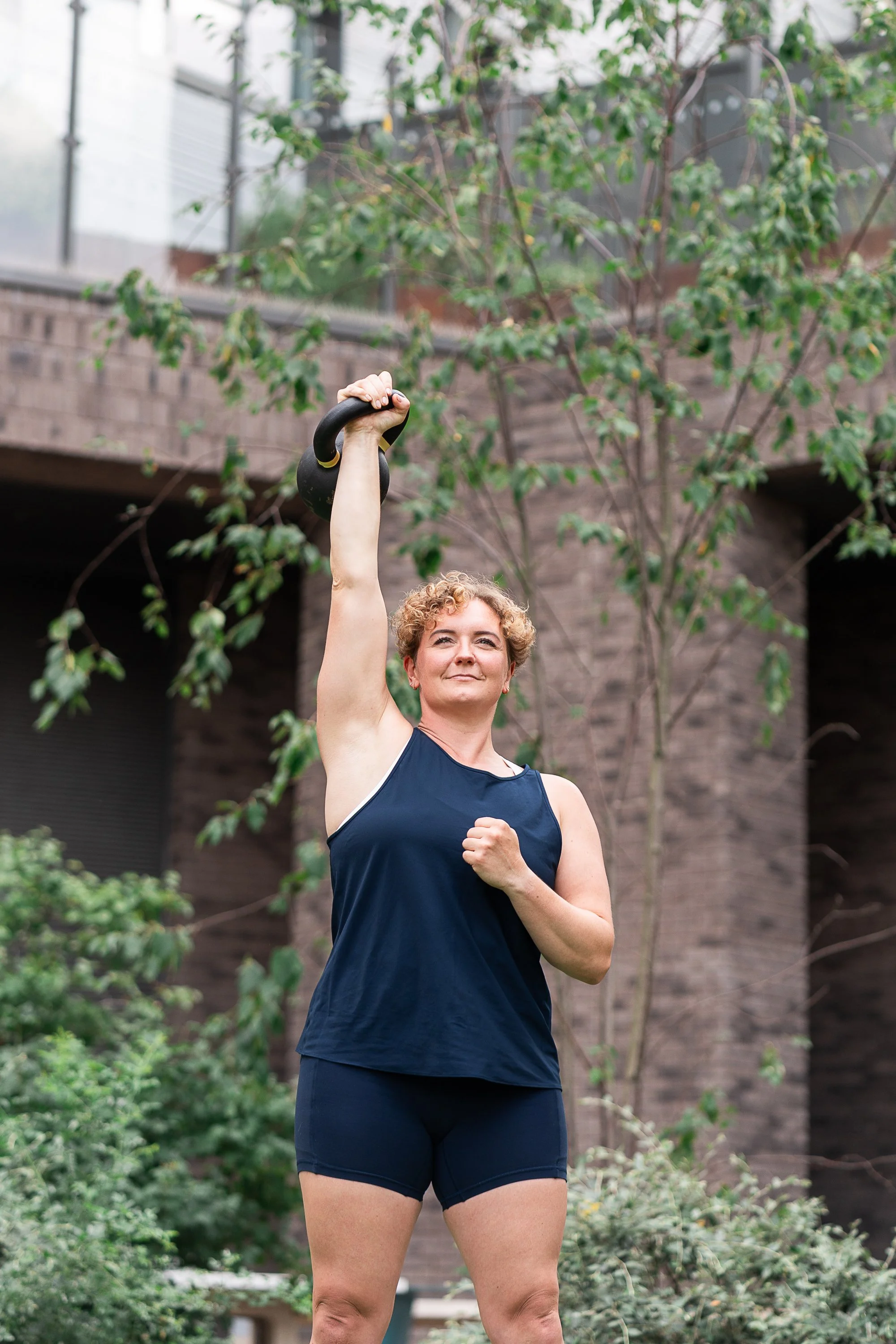 Personal trainer Rowena Ramsell lifting a kettlebell overhead during an outdoor strength workout
