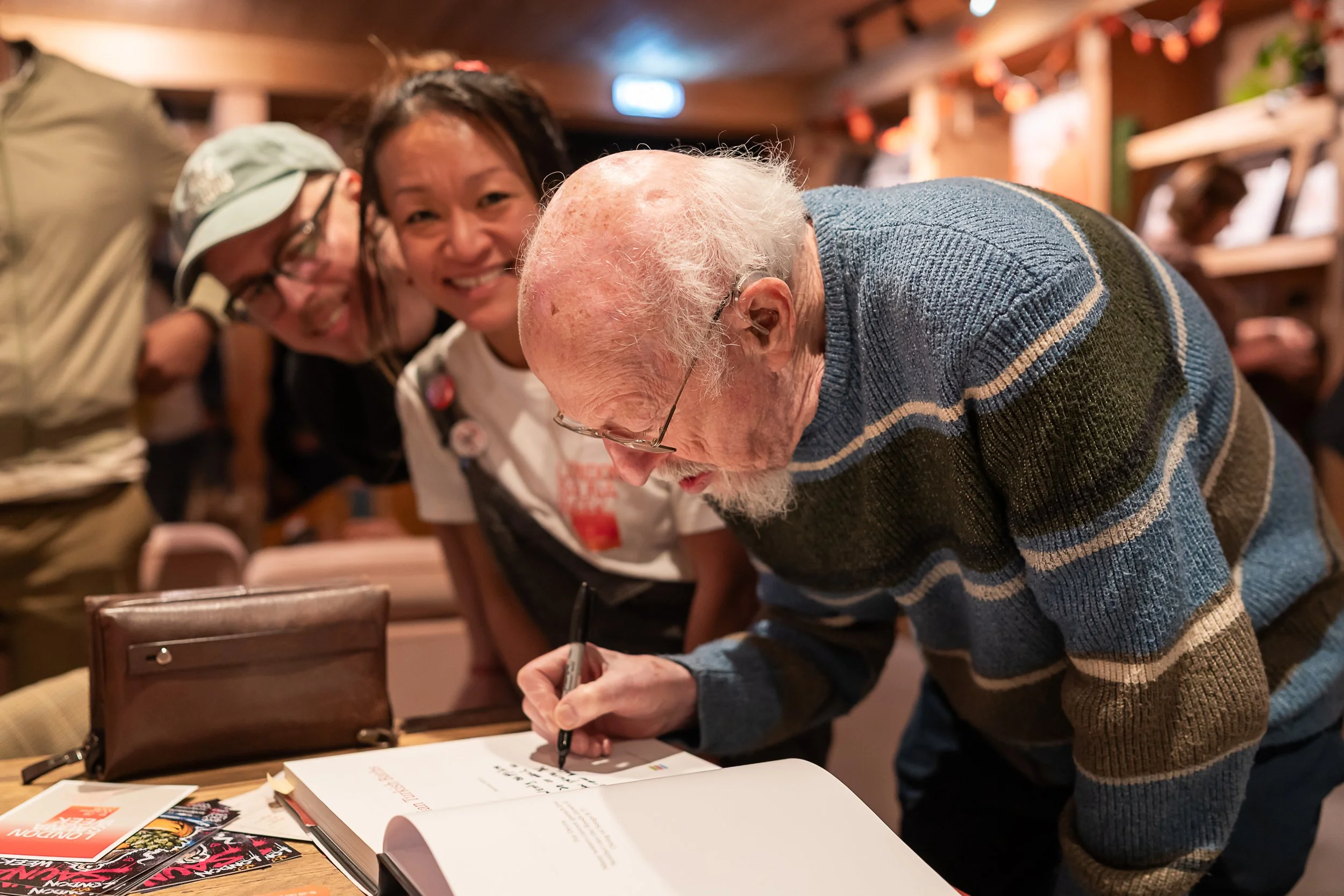 Malcolm Shifrin signing a book as co-founders Wendy Liu and Mika Meskanen look on