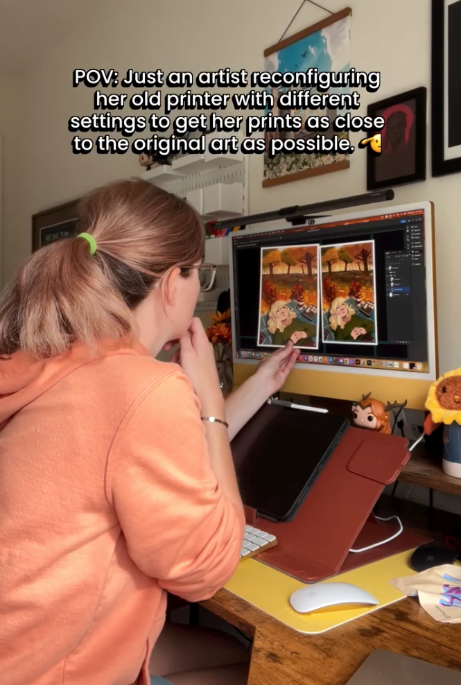 Show me the back of a woman, staring at her photo of a print, comparing it to how it looks on her digital screen