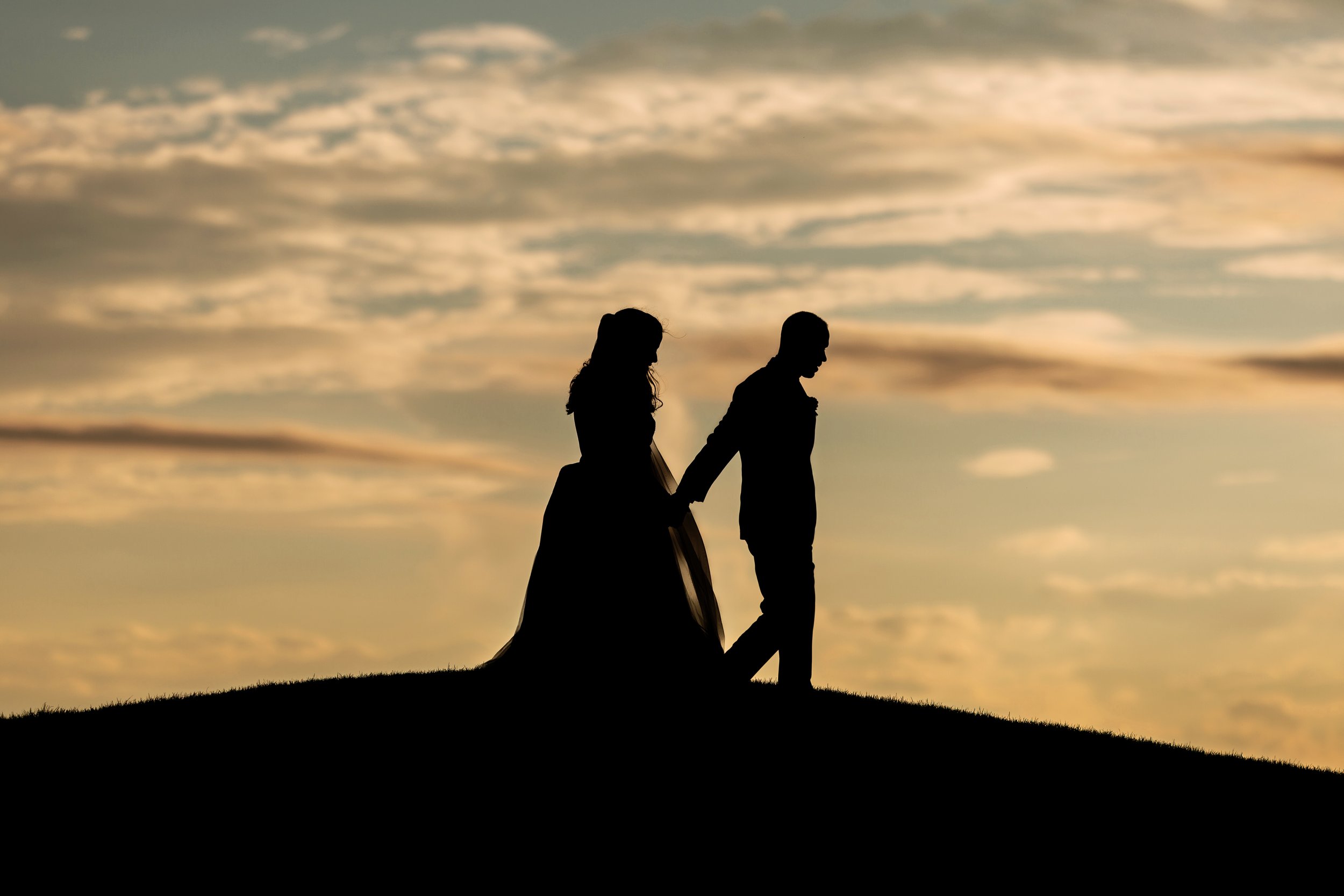  silhouette of bride and groom walk hand in hand at longuevue country club in front of a sunset 