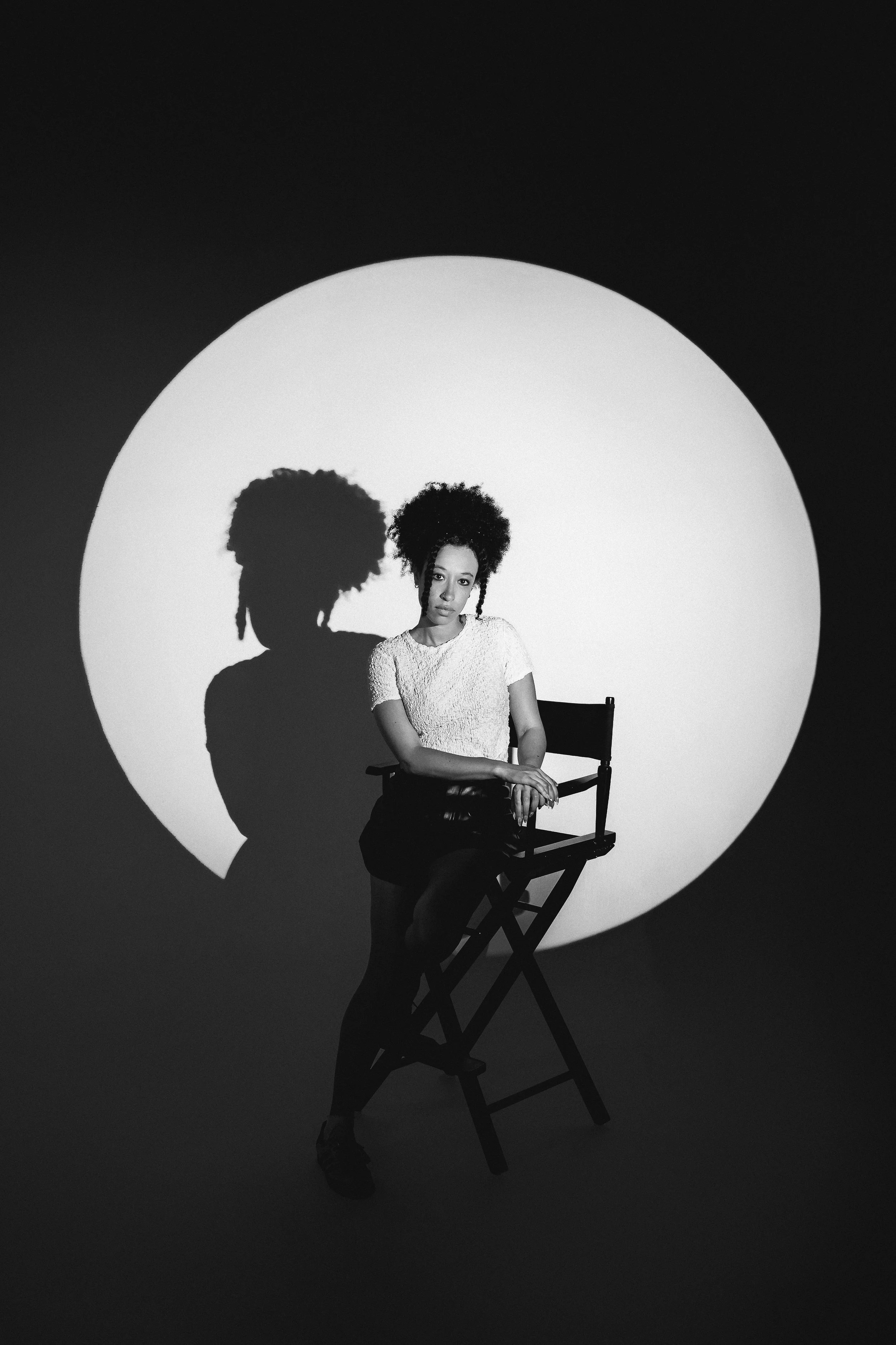 a woman sits on a director's chair in the middle of a spotlight at opya studios in pittsburgh