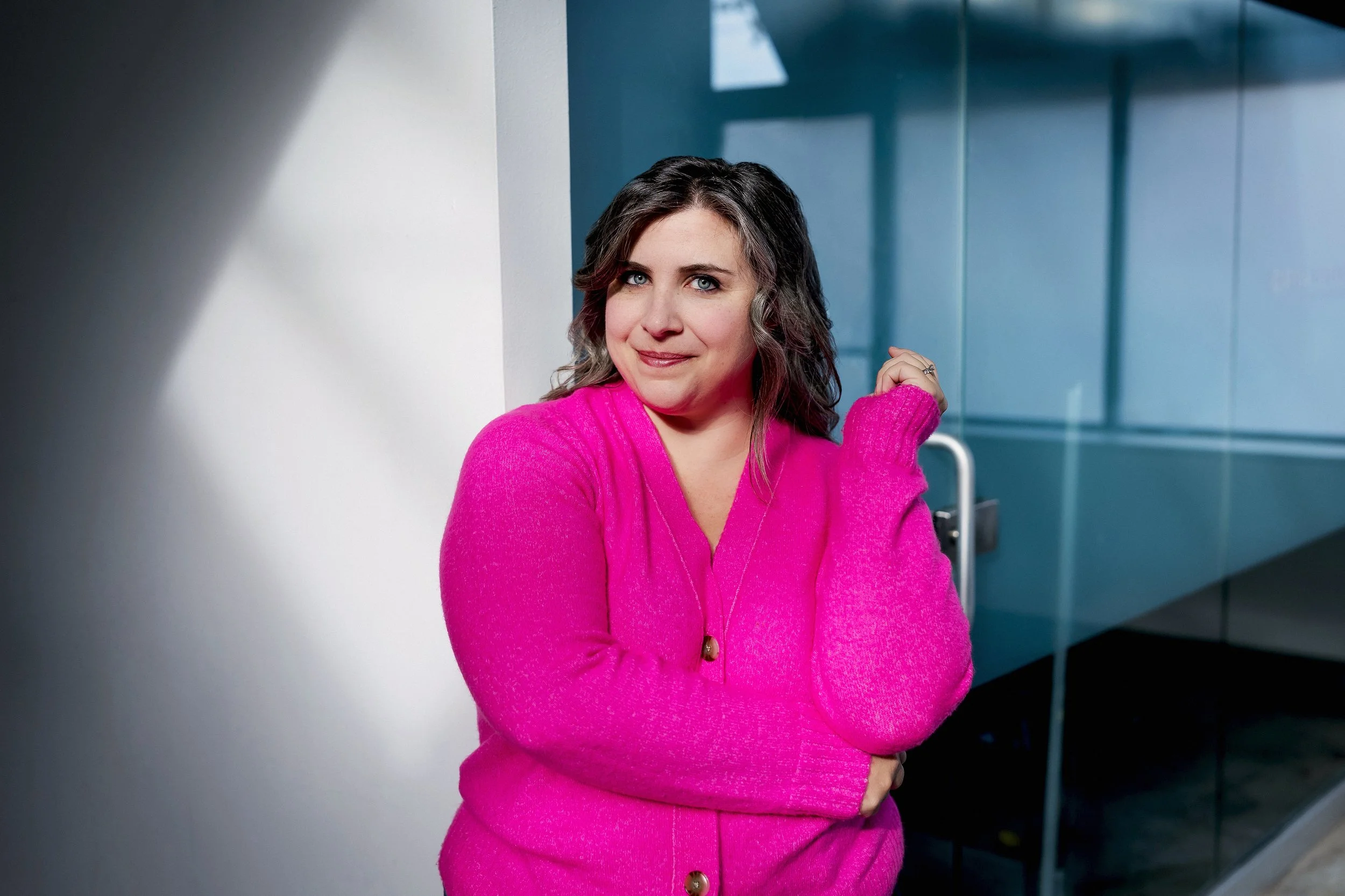 a pittsburgh actress wears a bright pink sweater against a glass door at opya studios in pittsburgh southside