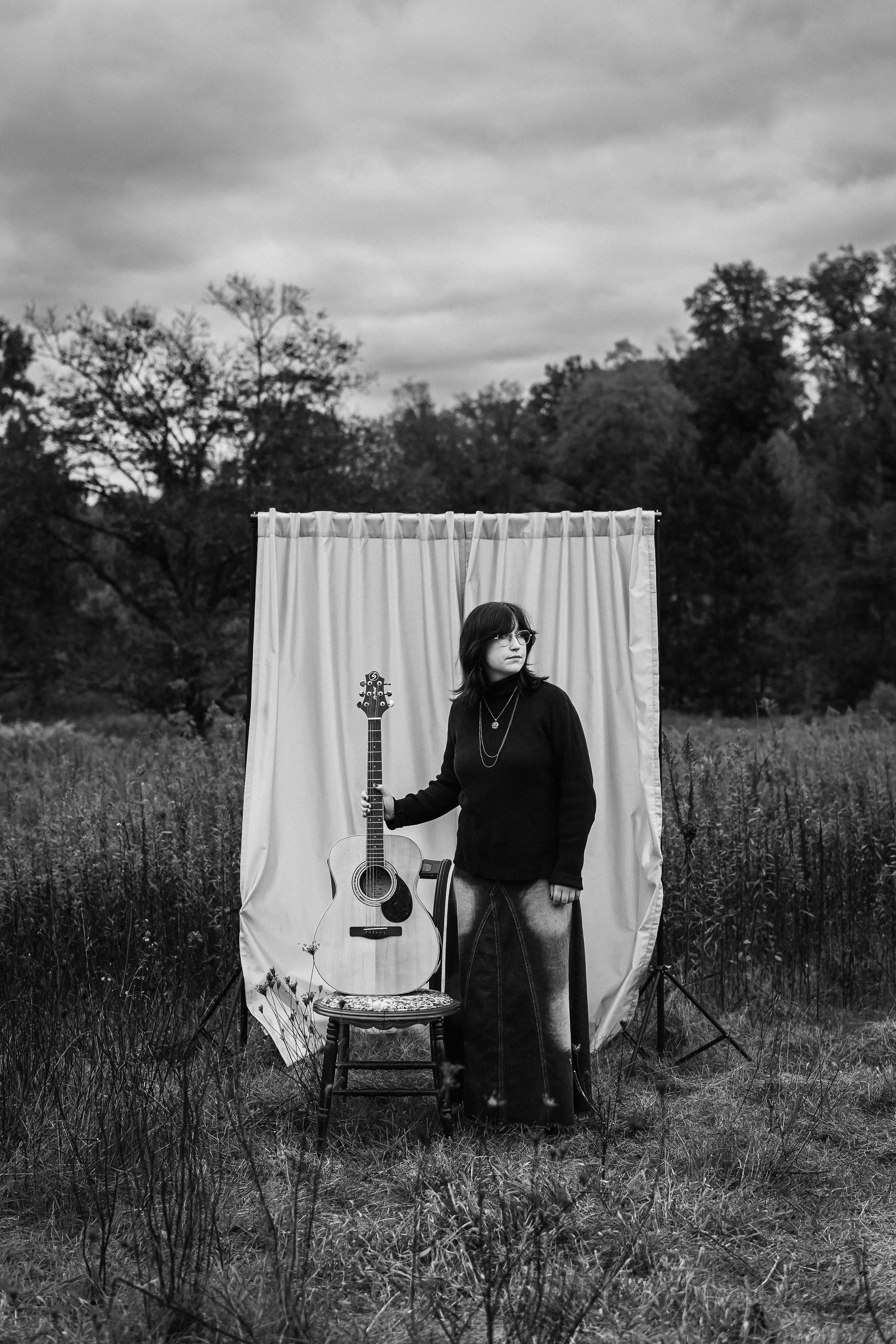 high school senior stands in front of an outdoor studio and rests her guitar on a chair at churchill valley greenway in pittsburgh