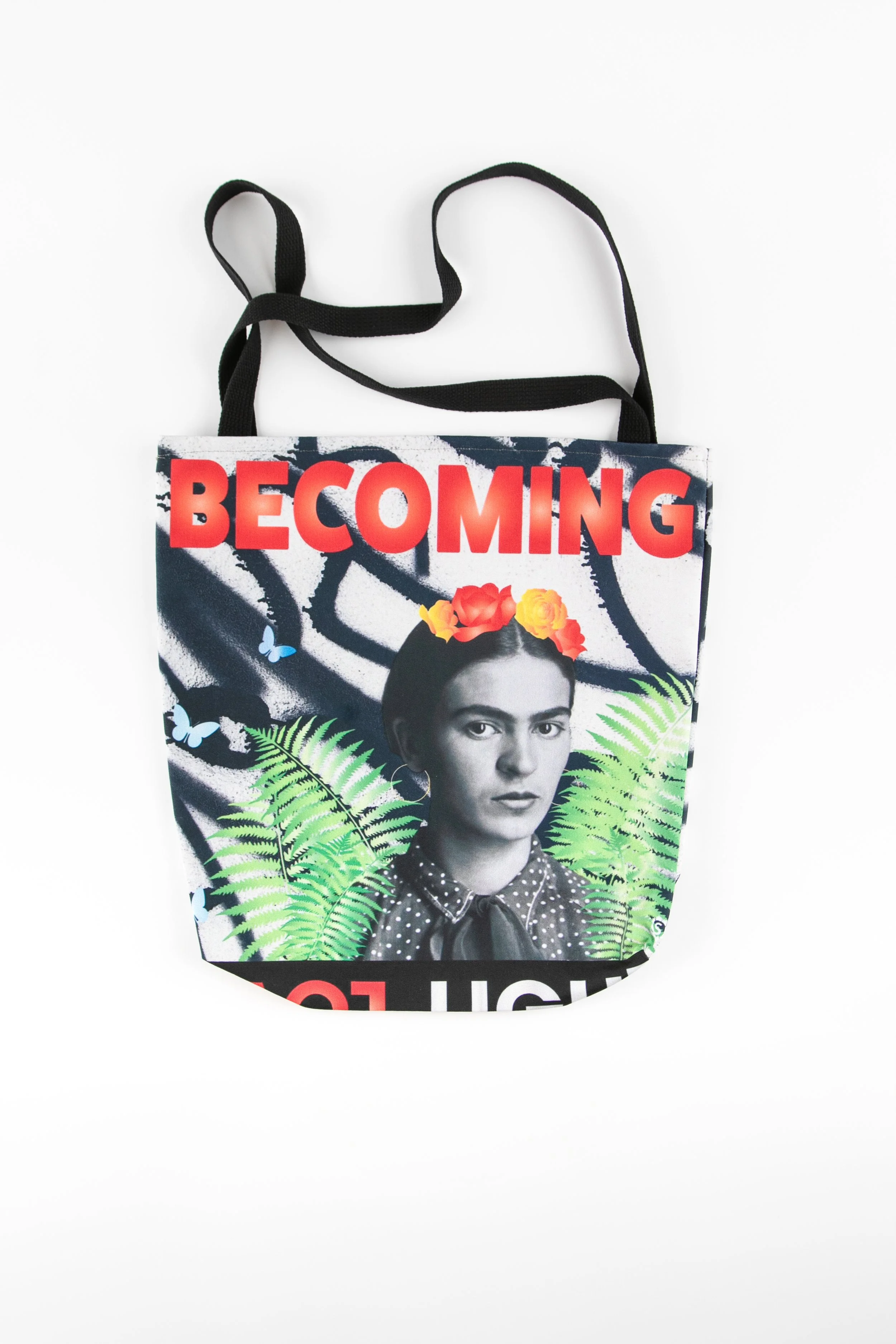 Art tote bag featuring a young Frida Kahlo in black and white with a crown of bright red and orange flowers, surrounded by green ferns, blue butterflies, and bold red “BECOMING” text on a monochrome abstract background.