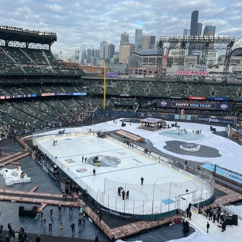 Ice hockey rink in a stadium with a city skyline in the background, preparing for a game or event.