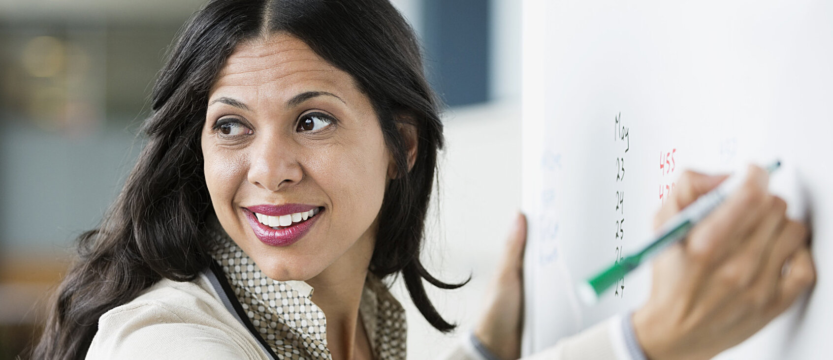 Smiling Latinx woman writing on white board