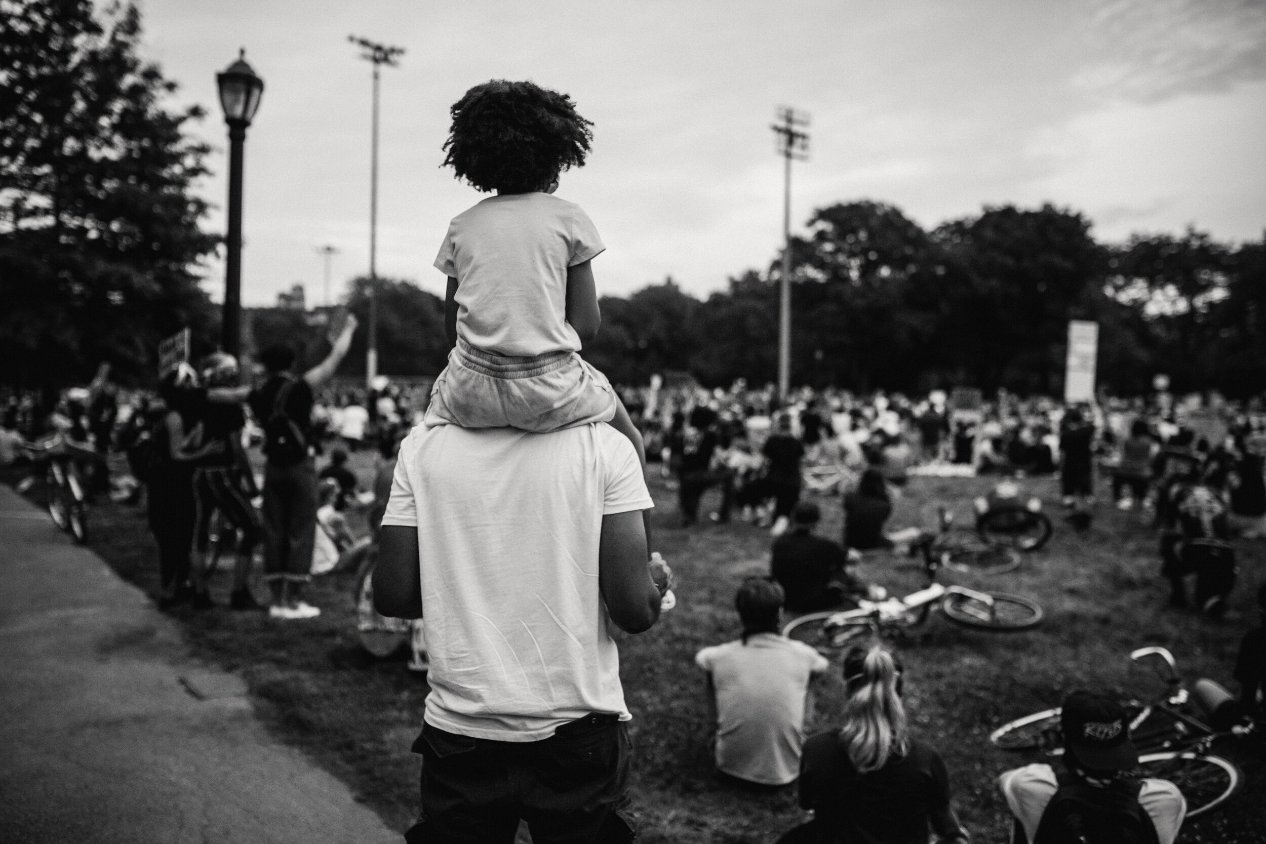 Young black girl perched atop man's shoulders watching a political rally