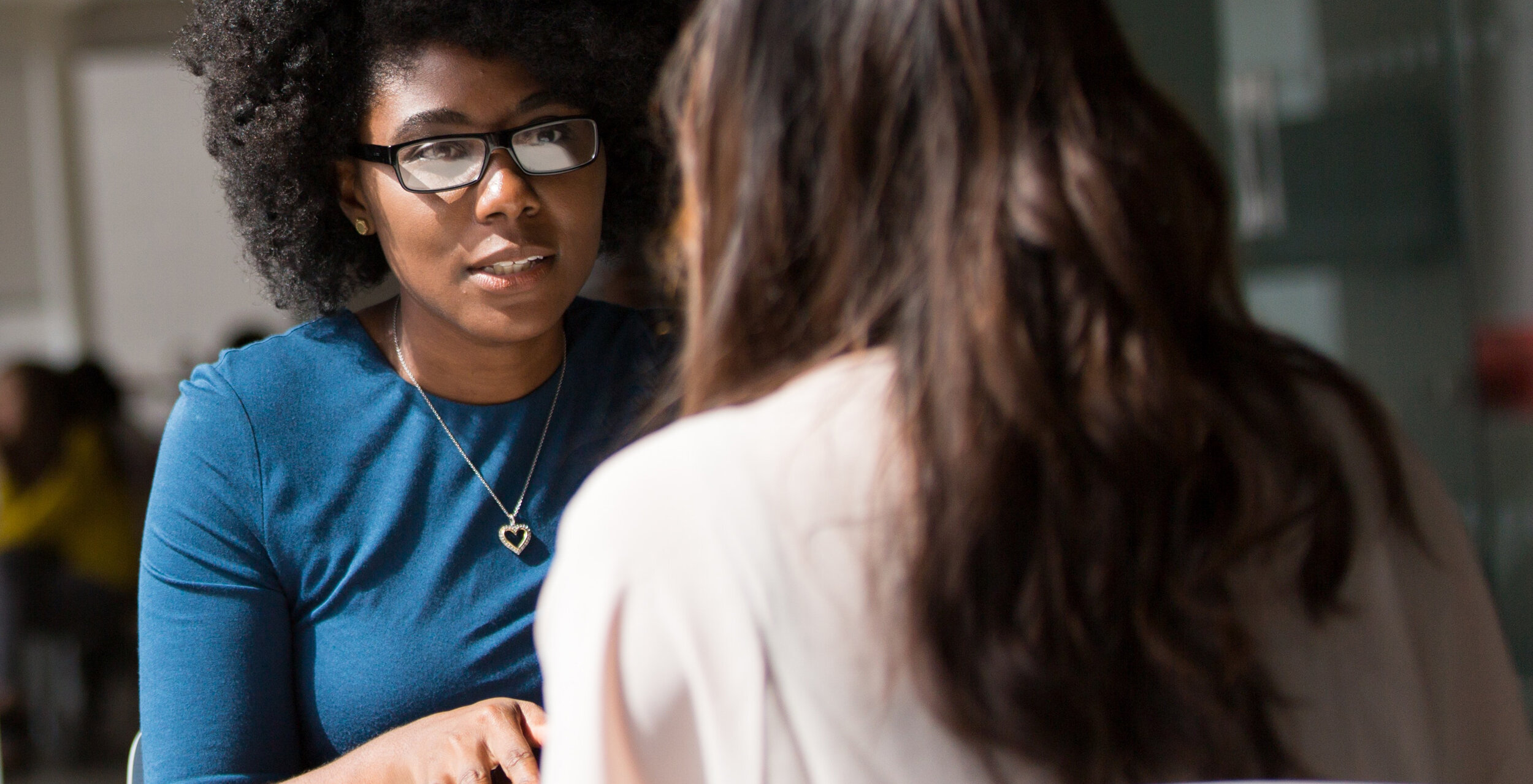 African American woman in blue top wearing heart pendant counseling another woman