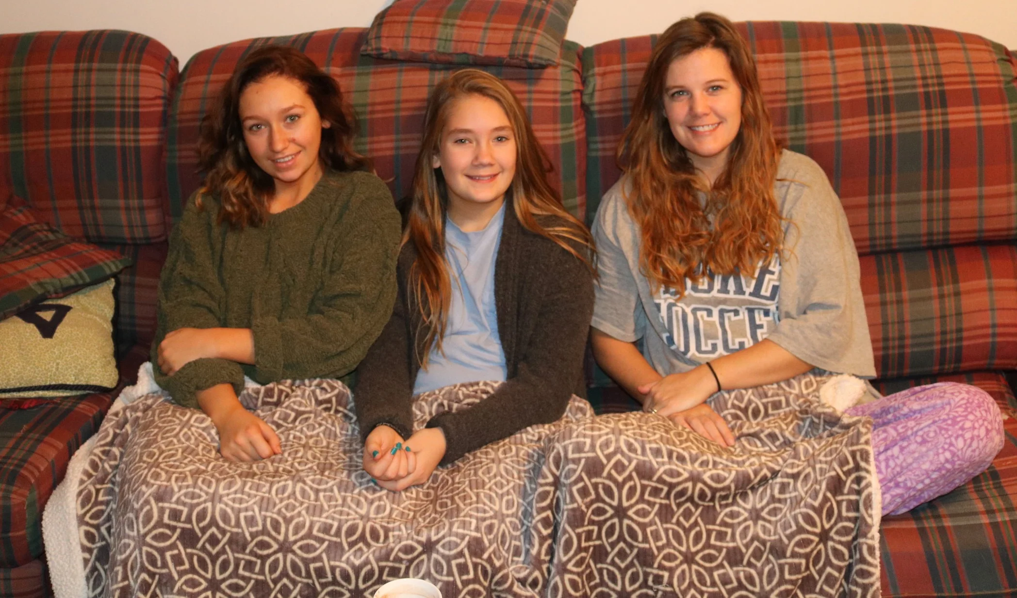 Maryellyn and the girls sharing the couch and a blanket on Christmas morning