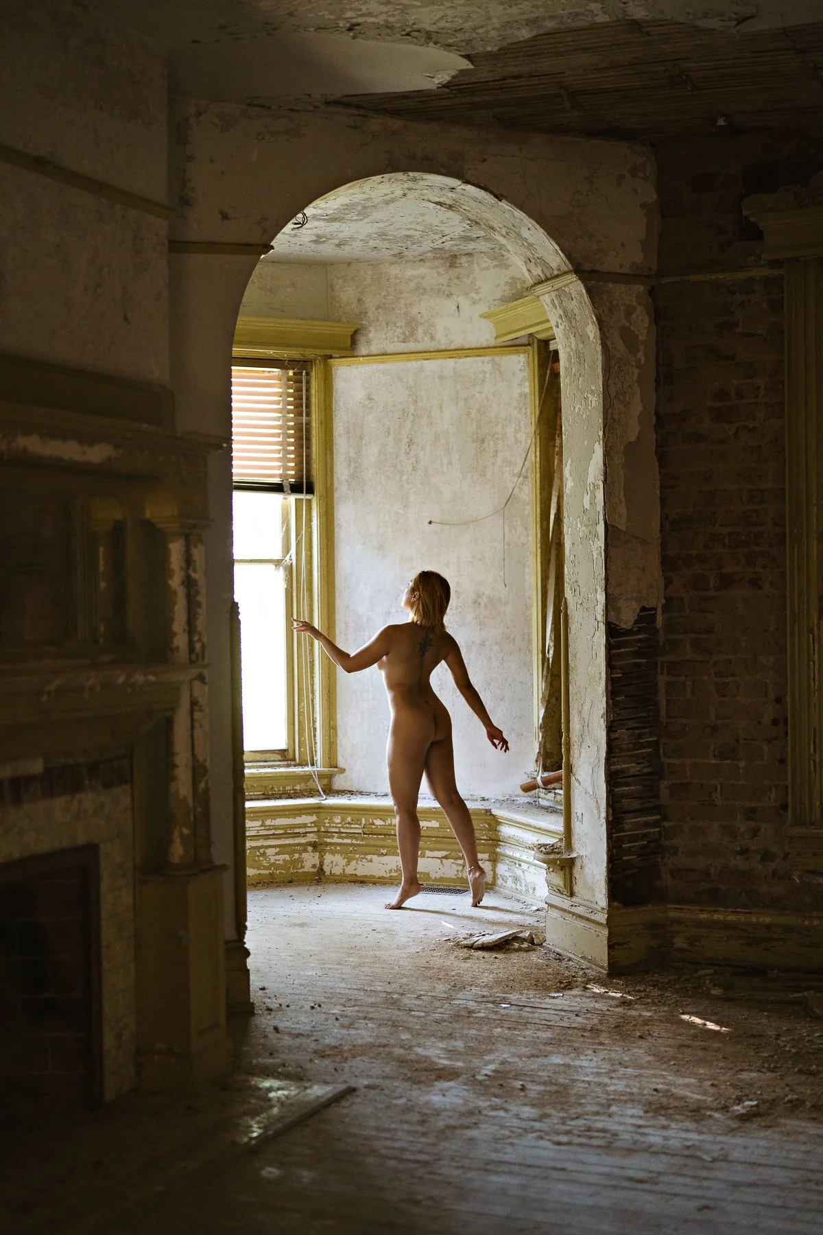 nude model posing in an archway in an abandoned mansion