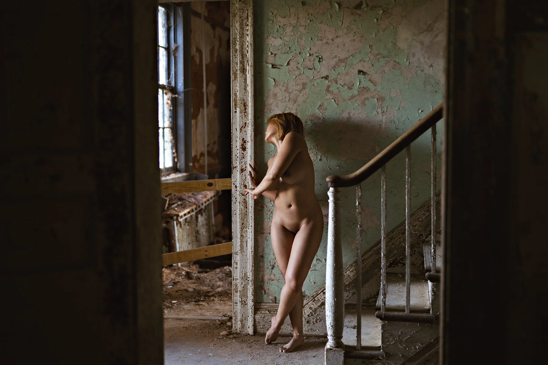 nude model posing at the bottom of a stair case in an abandoned mansion