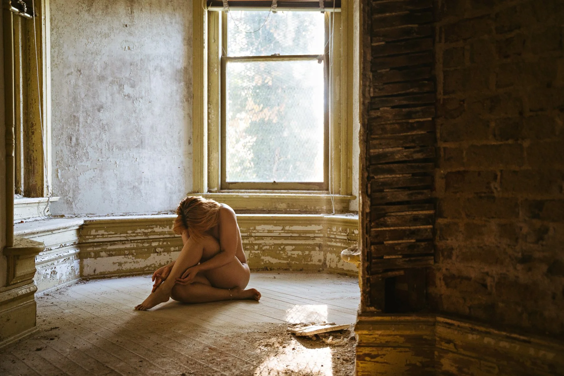 nude model posing in seated position in an abandoned mansion
