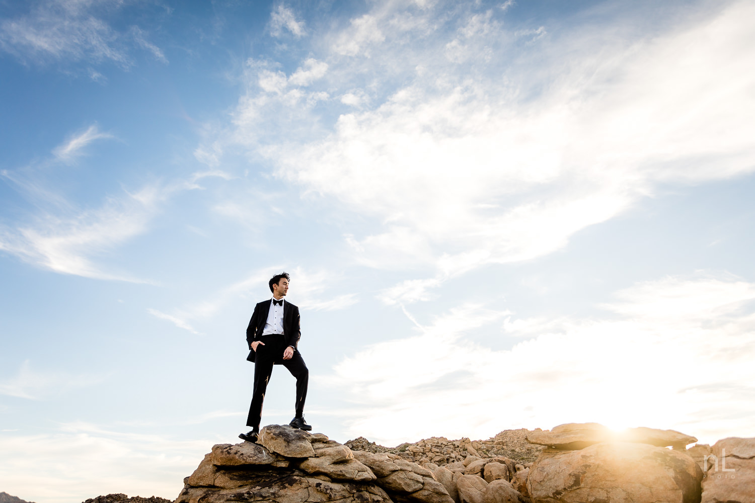 joshua-tree-engagement-wedding-elopement-photography-stylized-photoshoot-environmental-portrait-groom-on-rock-formation-sunset-clouds