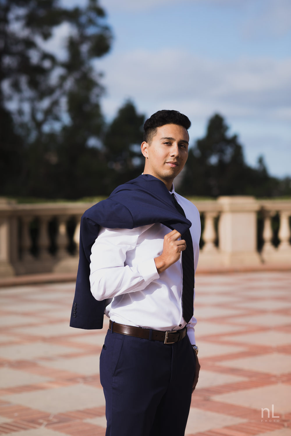 UCLA Class of 2019 graduate wearing suit and tie and graduation sash smiling and standing in front of Royce Hall.