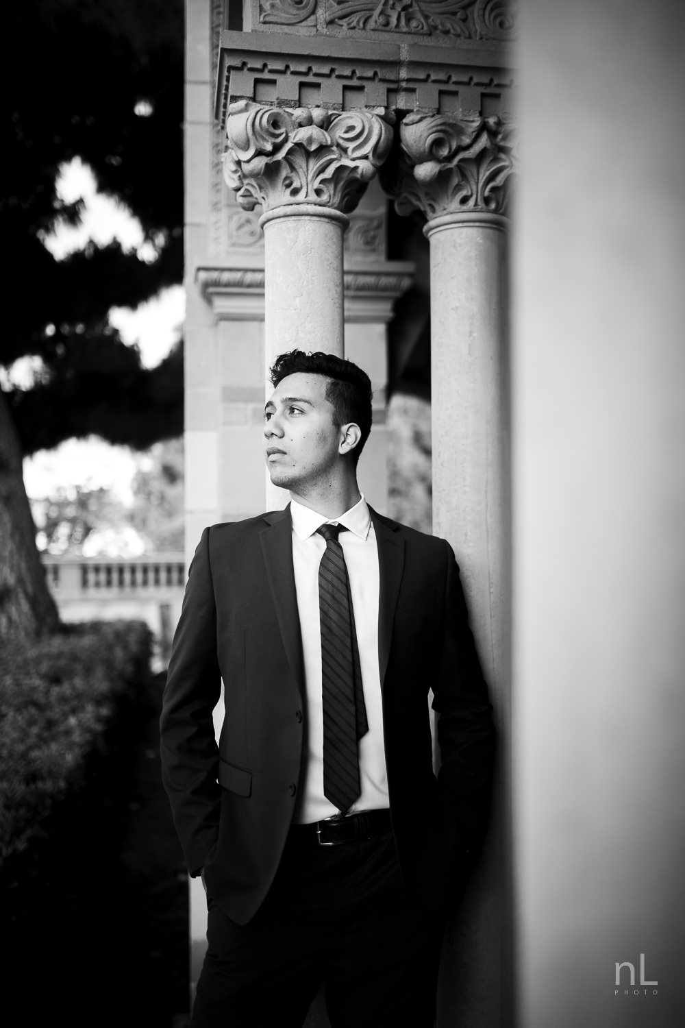 UCLA Class of 2019 graduate wearing suit and tie and graduation sash smiling and standing in front of Royce Hall.