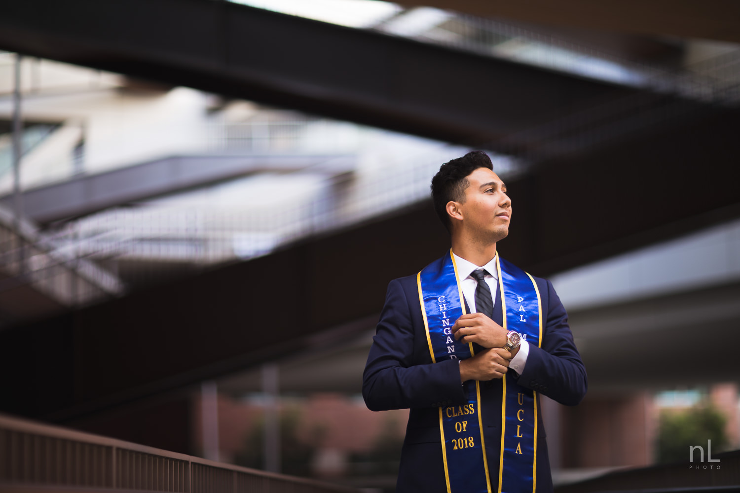 UCLA Class of 2019 graduate wearing suit and tie and graduation sash adjusting watch and smiling.