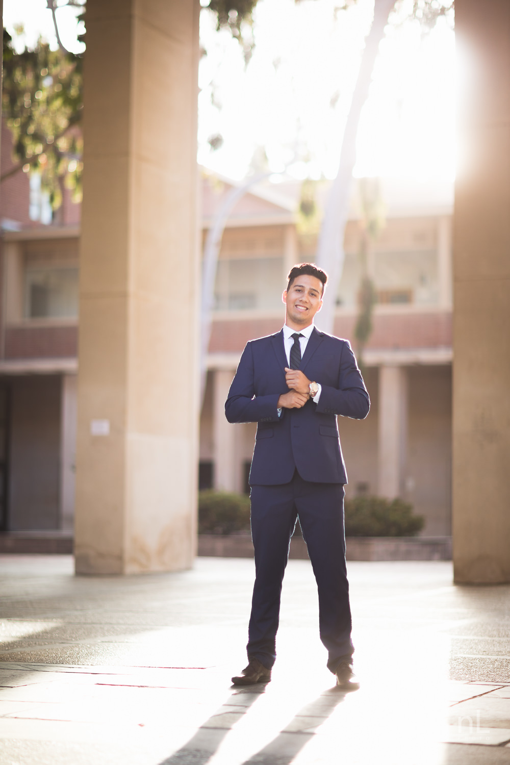 UCLA Class of 2019 graduate wearing suit and tie and graduation sash looking serious in front of Young Hall.