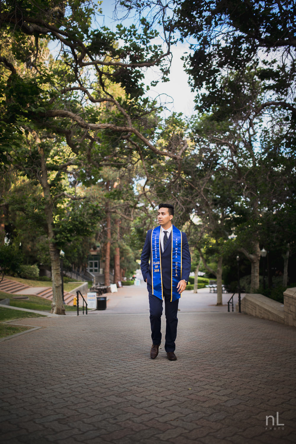 UCLA Class of 2019 graduate wearing suit and tie and graduation sash walking down Bruinwalk.