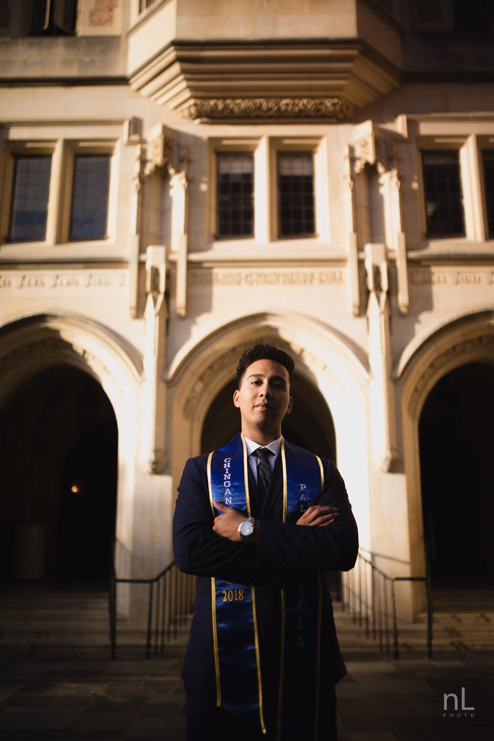 UCLA Class of 2019 graduate wearing suit and tie and graduation sash looking serious in front of Kerckhoff Hall.