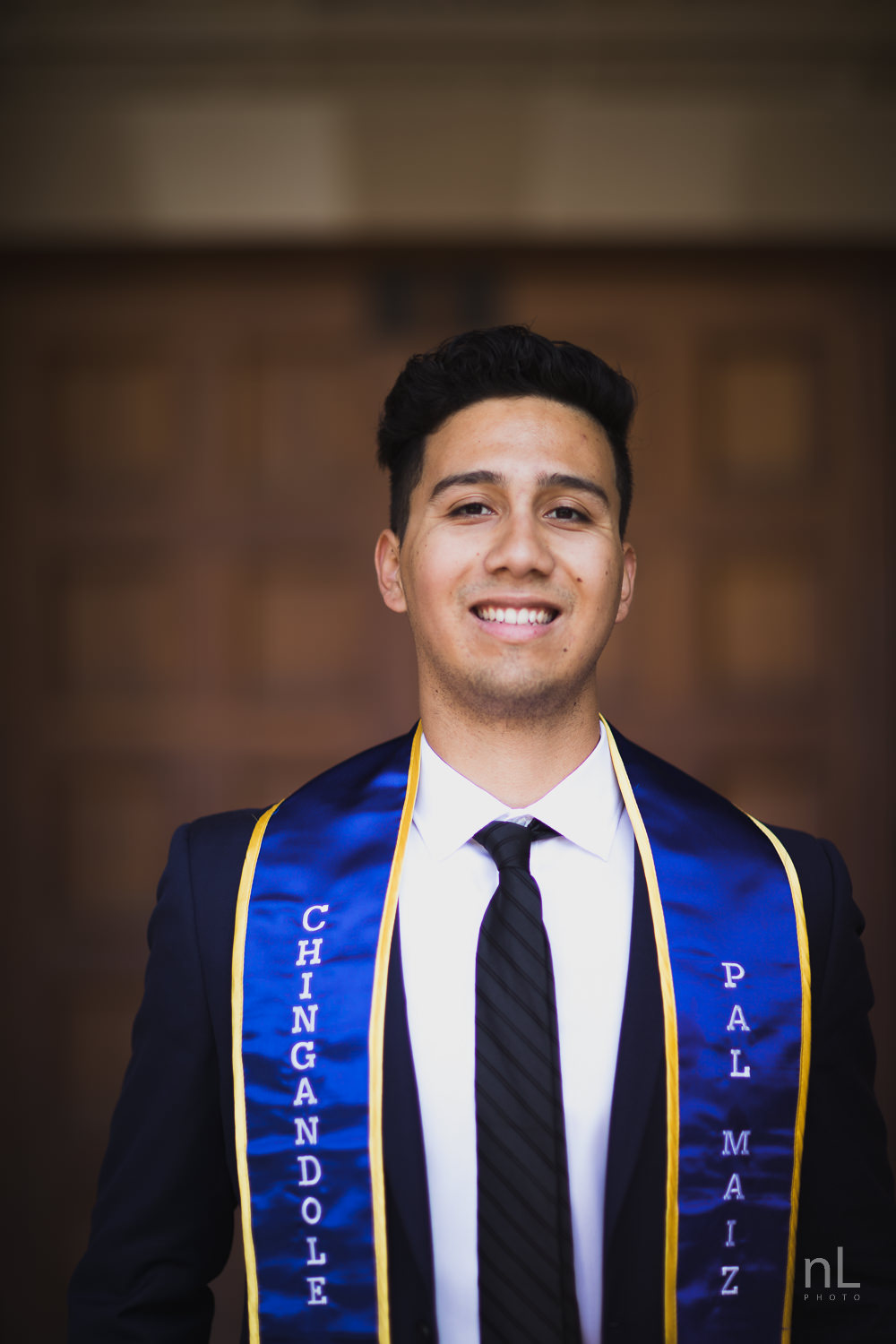 UCLA Class of 2019 graduate wearing suit and tie and graduation sash smiling and standing in front of Royce Hall.