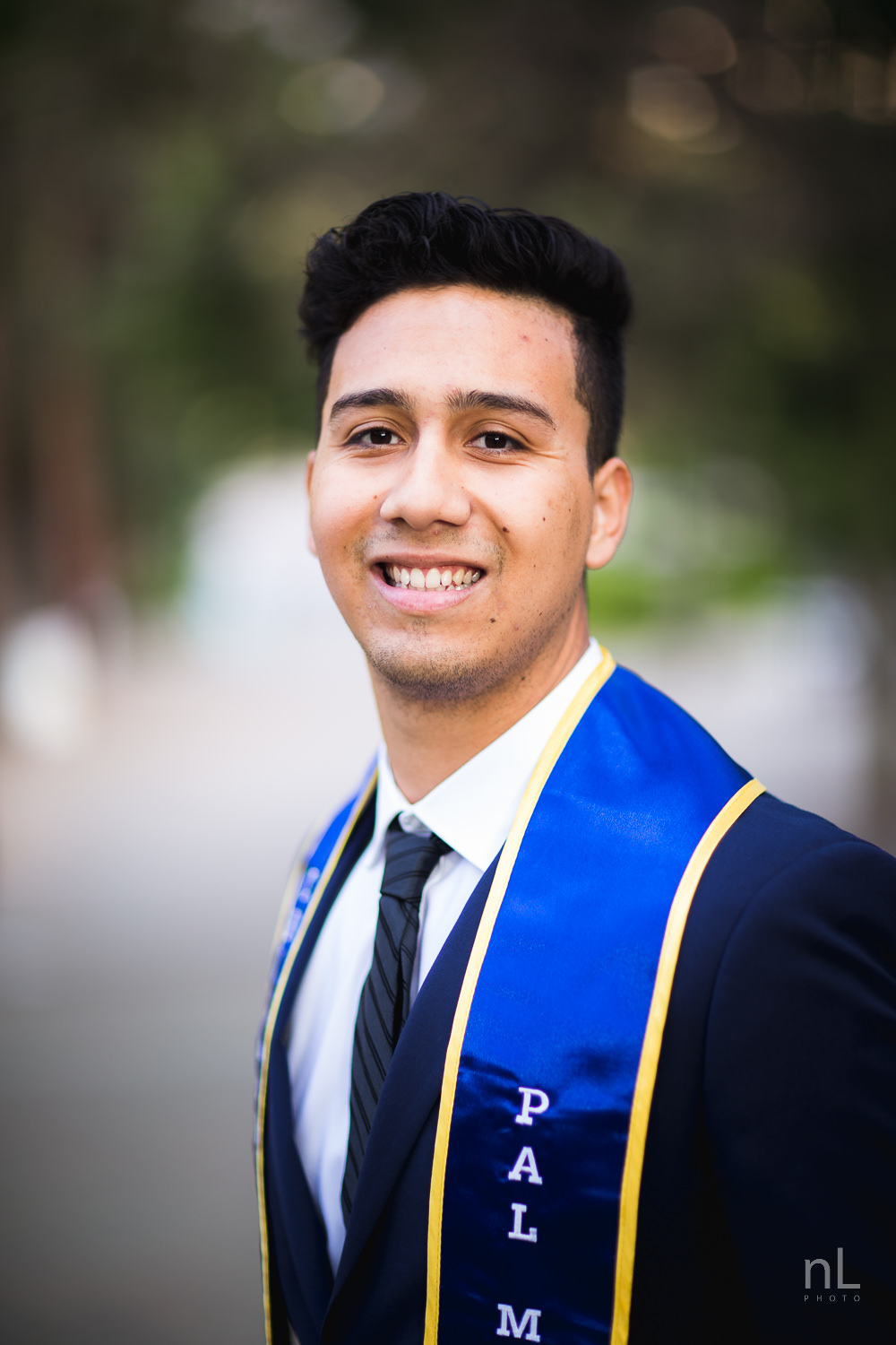 UCLA Class of 2019 graduate wearing suit and tie and graduation sash walking down Bruinwalk.